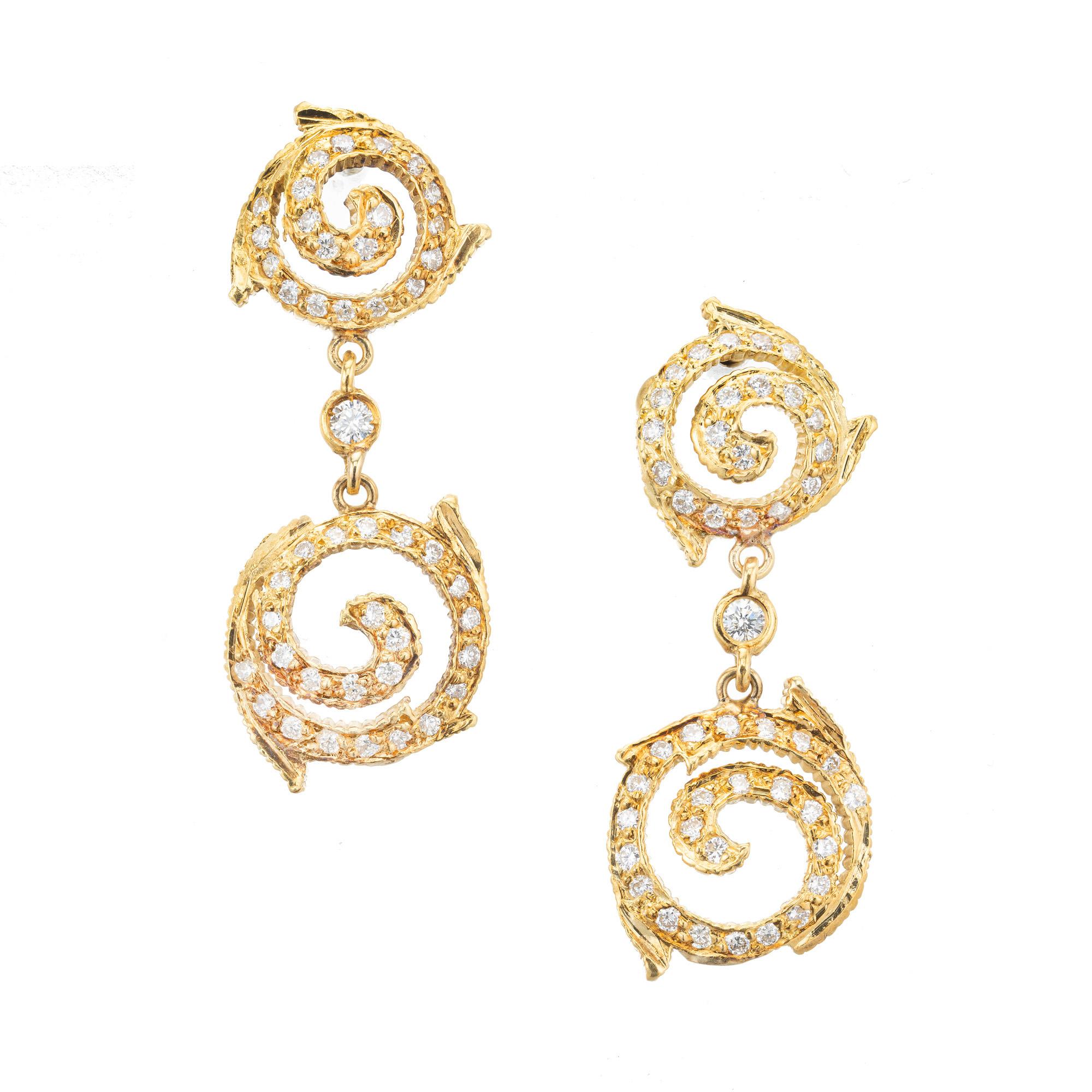 Created by Doris Panos these 18k yellow gold dangle earrings are adorned with 90 full cut diamonds approximately totaling .90cts. and graded G near colorless with a clarity of VS2-Si1. The two unique diamond swirl sections are connected by a round