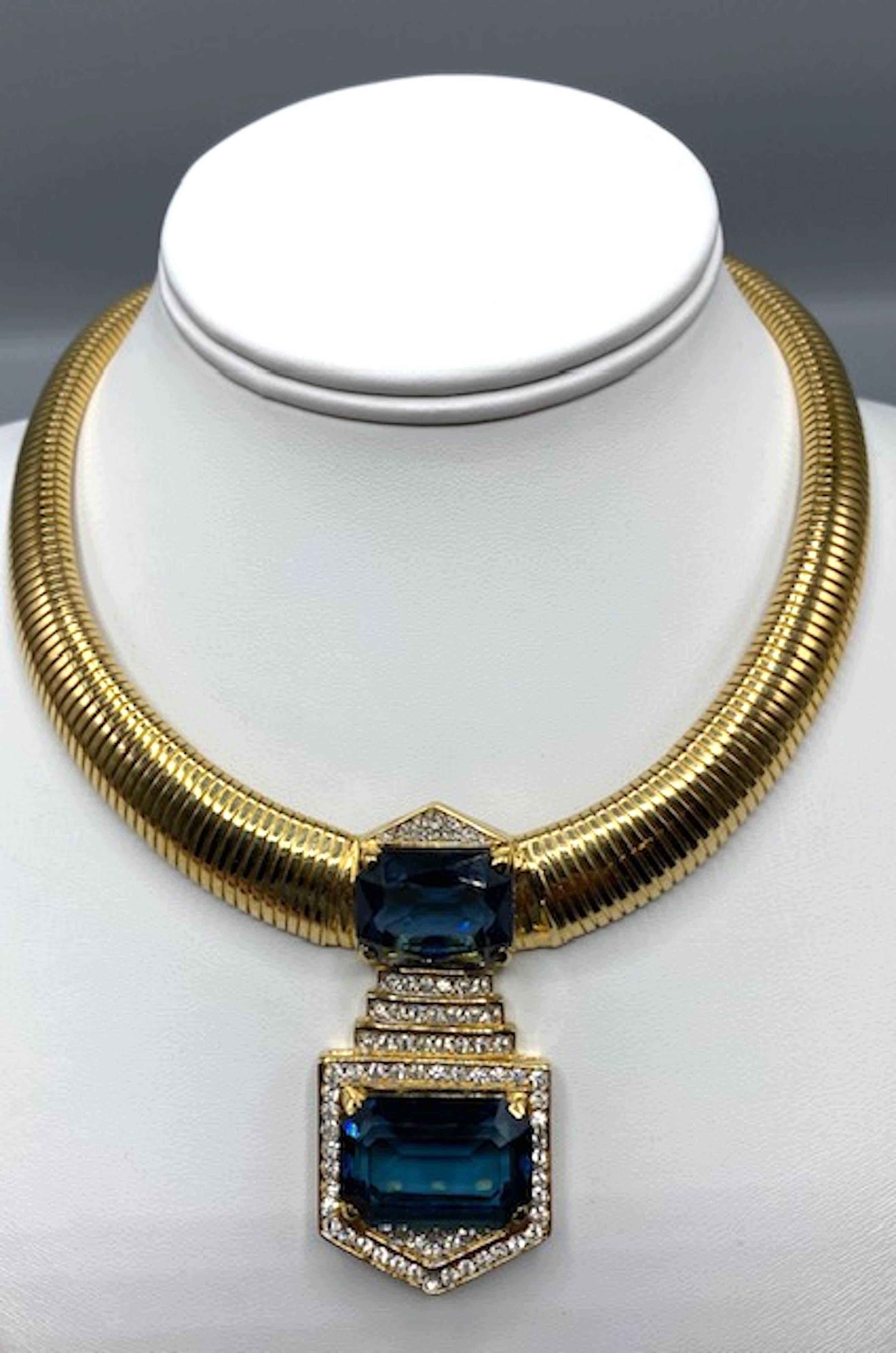 A lovely quality Omega-style Art Deco Style necklace by the high-end Canadian costume jeweller D'Orlan. Gold plated, pave rhinstone on the pendant, with two cushion cut blue stone in the center.
Very fine condition.
Stamped D'ORLAN on the pendant,