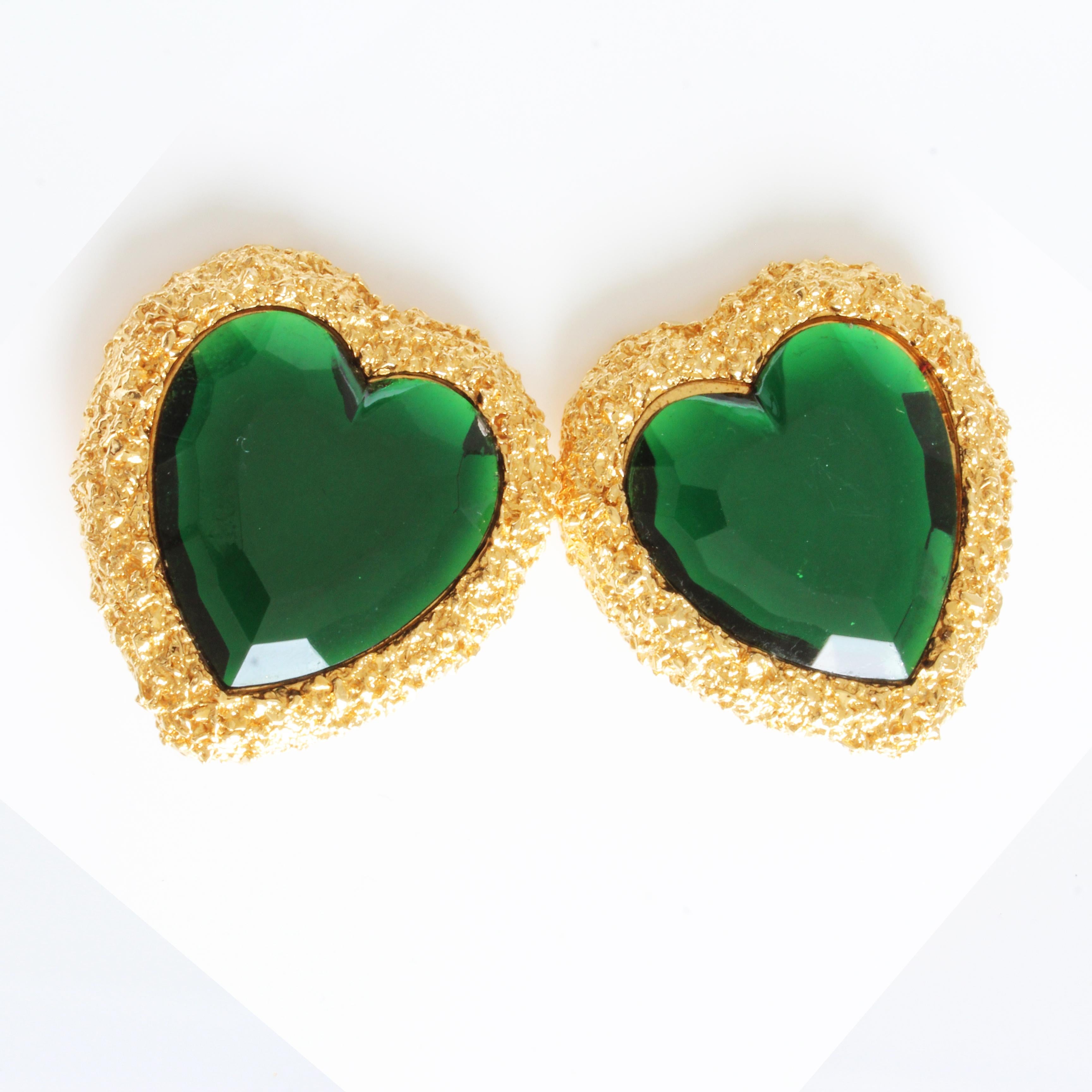 These massive gold tone and emerald crystal heart-shaped earrings were made by D'Orlan, manufacturer of costume pieces for Nina Ricci and Lancel, most likely in the 1980s. Made from gold textured metal settings, they feature emerald green colored,
