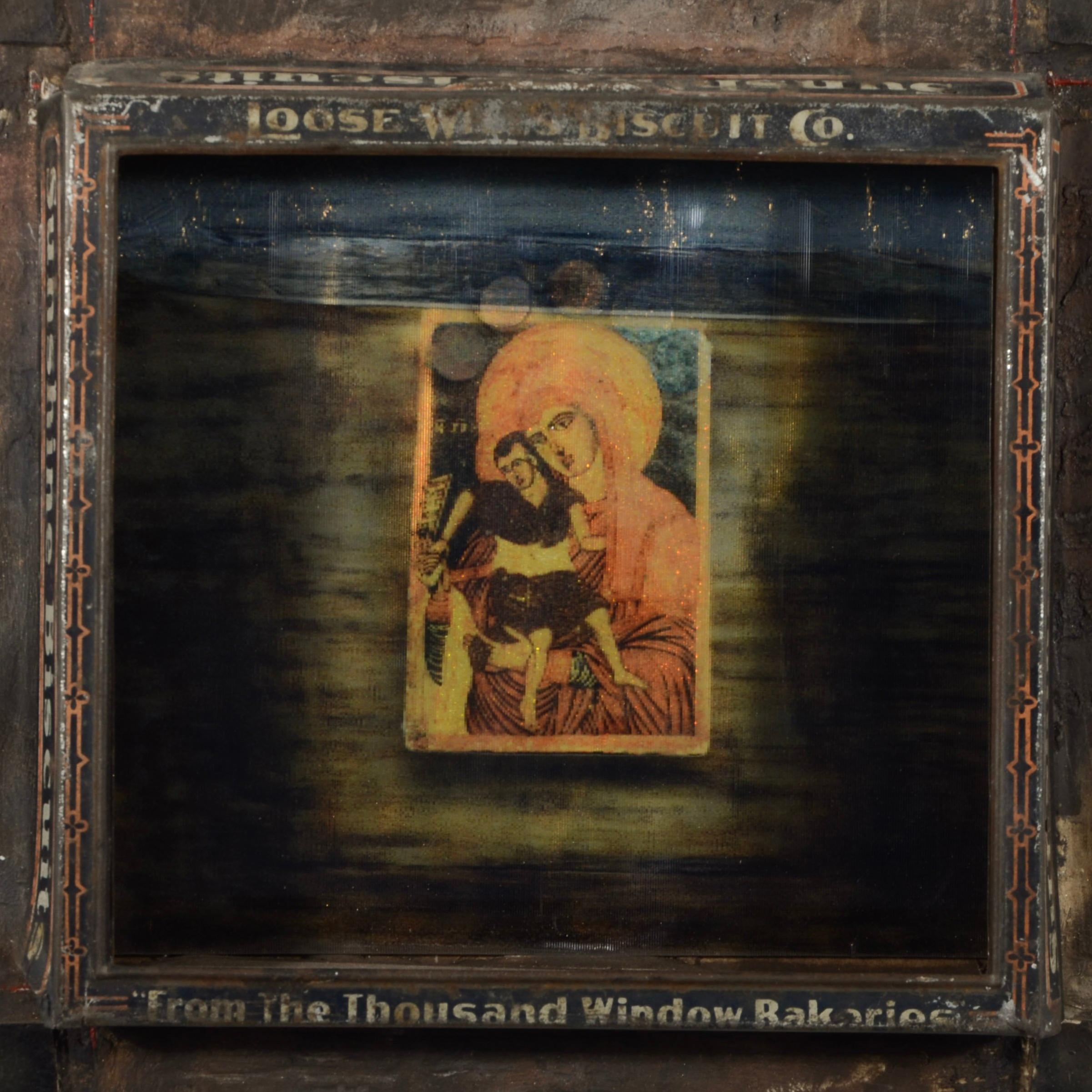 Dorothy Simpson Krause’ “Under Glass” is a 12 x 12 x 3 inch wall-based assemblage incorporating a vintage ‘Sunshine Biscuits’ tin and a found image of the Madonna and child behind a lenticular lens at the center of the piece.  The tin works as a