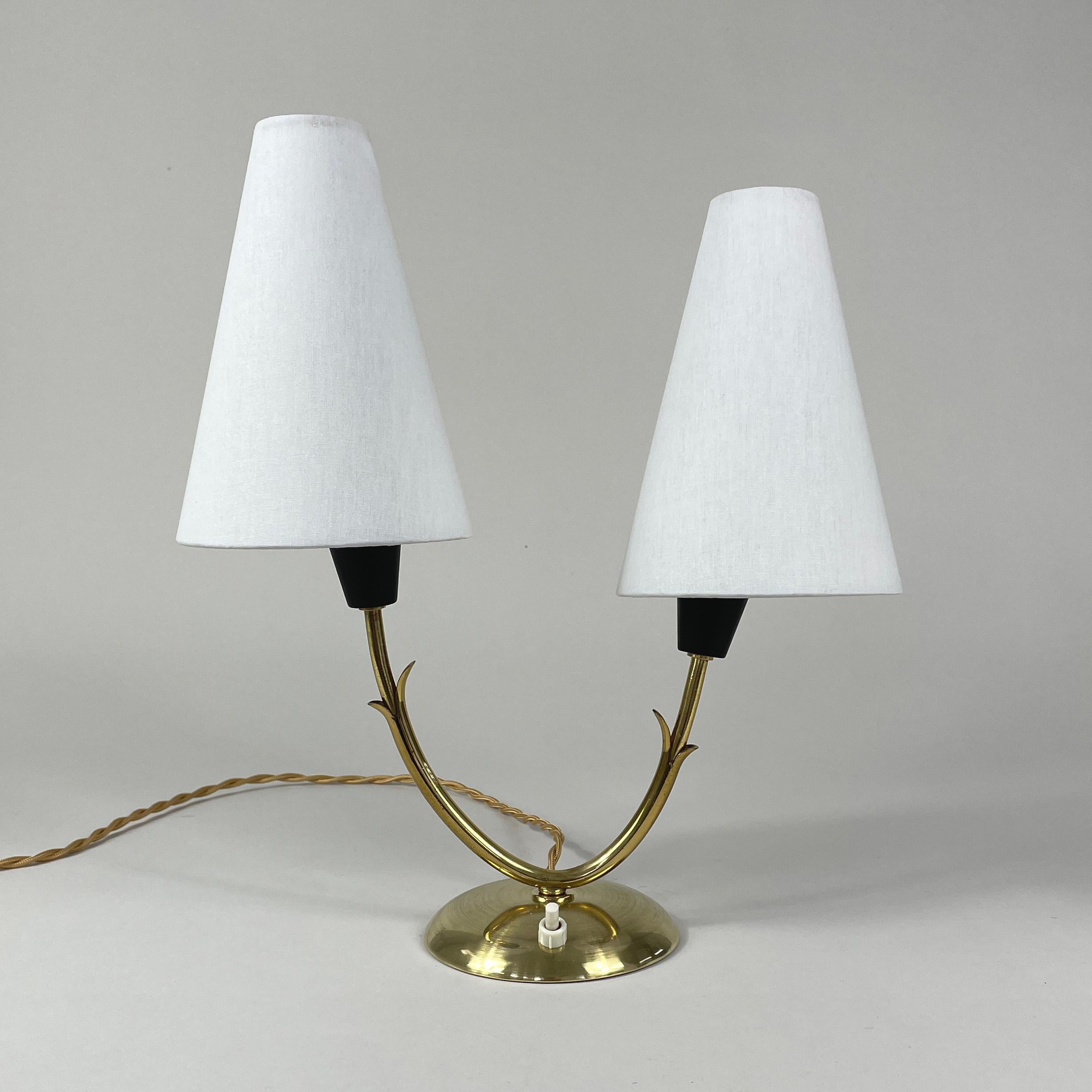 Cette lampe de table inhabituelle à double bras a été conçue et fabriquée en Suède dans les années 1950. Elle se compose d'une base en laiton et d'un abat-jour en lin blanc cassé à clipser. Les abat-jour peuvent être déplacés dans différentes