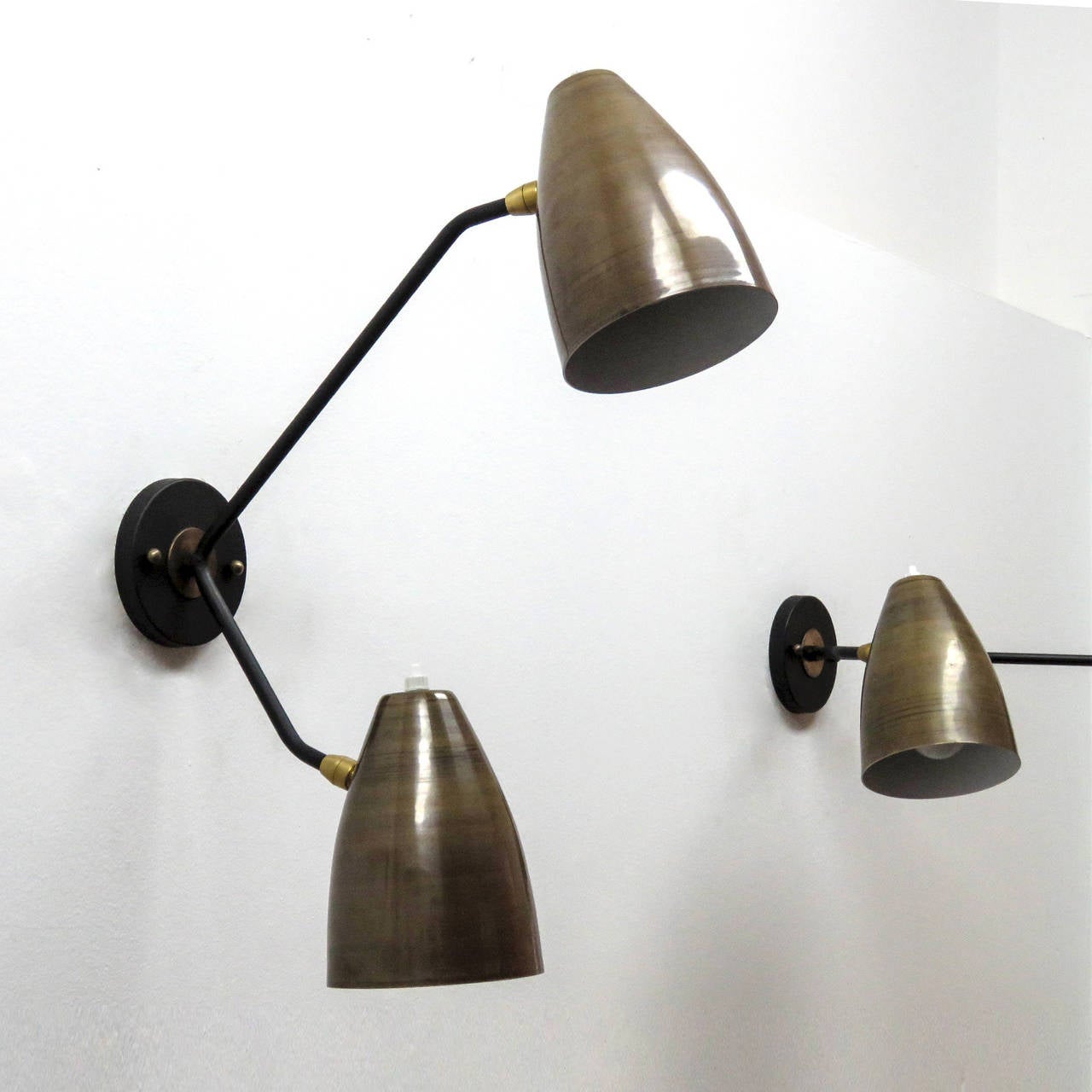 Wonderful asymmetrical double arm wall lights by Gallery L7, handcrafted and finished in Los Angeles with two fully adjustable raw brass shades with white enameled interiors on black enameled arms, can be mounted vertically or horizontally, each