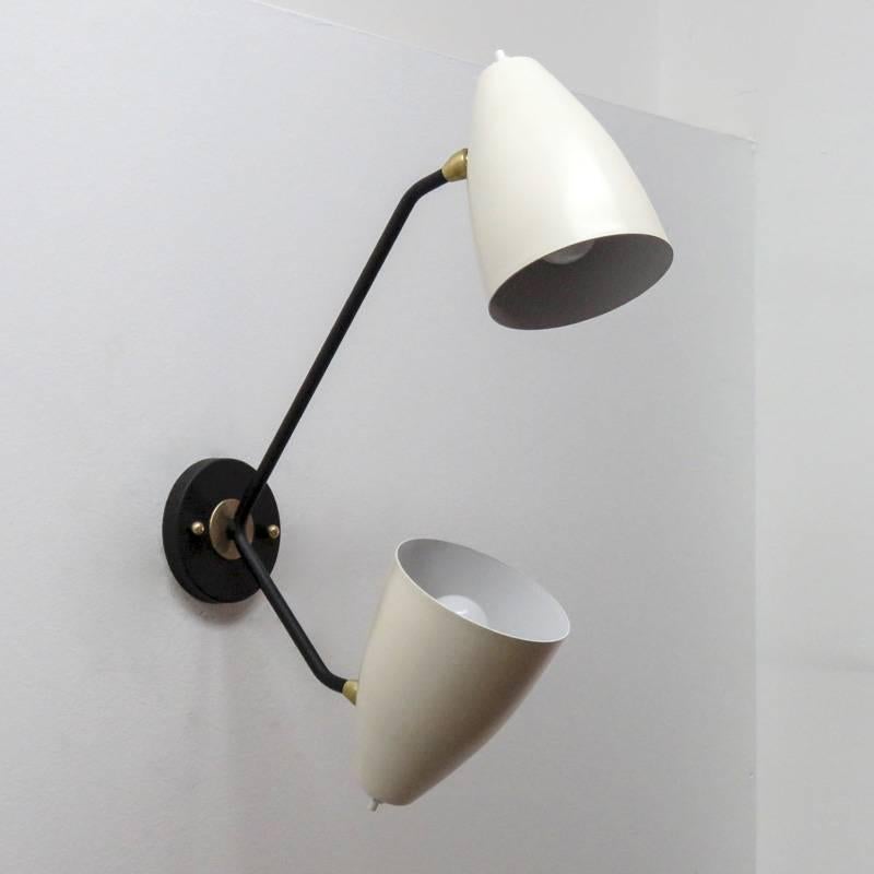 Wonderful asymmetrical double arm wall lights, two fully adjustable two-tone brass shades (egg shell with white enameled interiors) on black enameled arms, can be mounted vertically or horizontally, each shade with individual on and off switch. Two