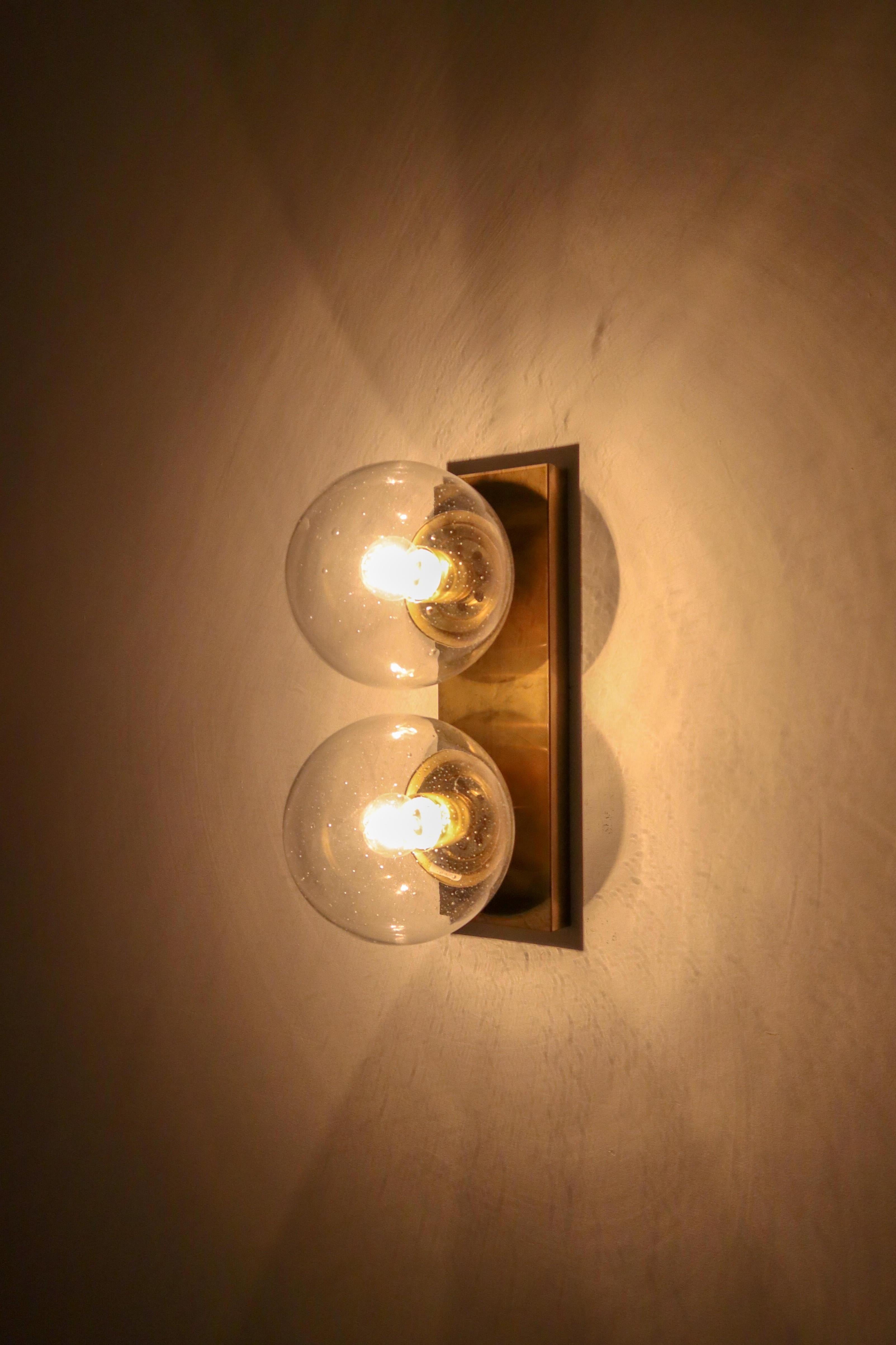 Double wall sconces with rectangular backplate and hand blowed glass globes. The bulbs are connected directly to a brass vertical slat that is connected directly to the wall. The pleasant light it spreads is very atmospheric; these wall scones will