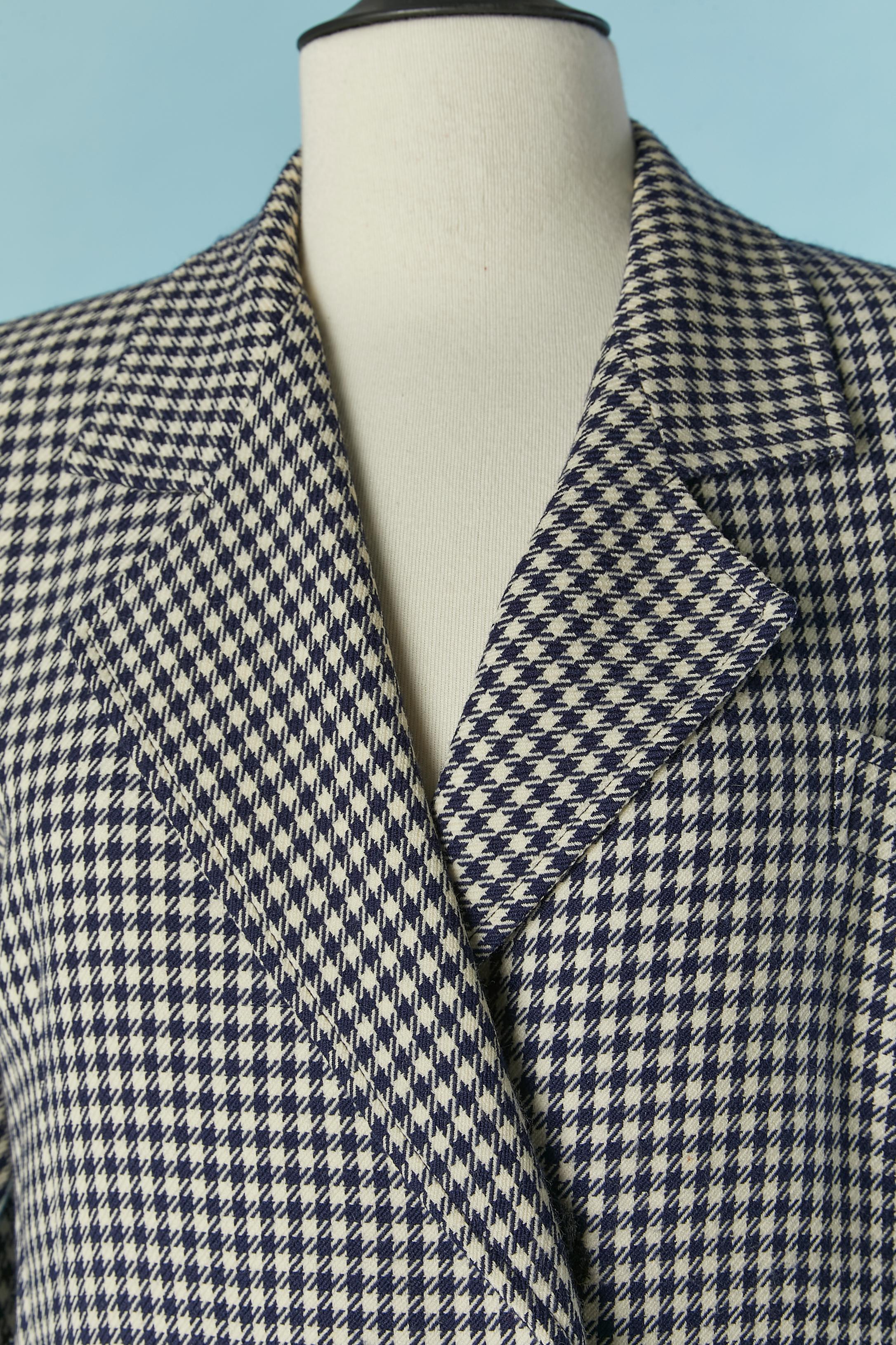 Cappotto doppiopetto con motivo pied-de-poule in bianco e blu. Non c'è l'etichetta della composizione del tessuto, ma il tessuto principale è la lana e la fodera l'acetato o il rayon. 
Spallaccio. Chiusura con bottoni e asole sul font centrale e sui