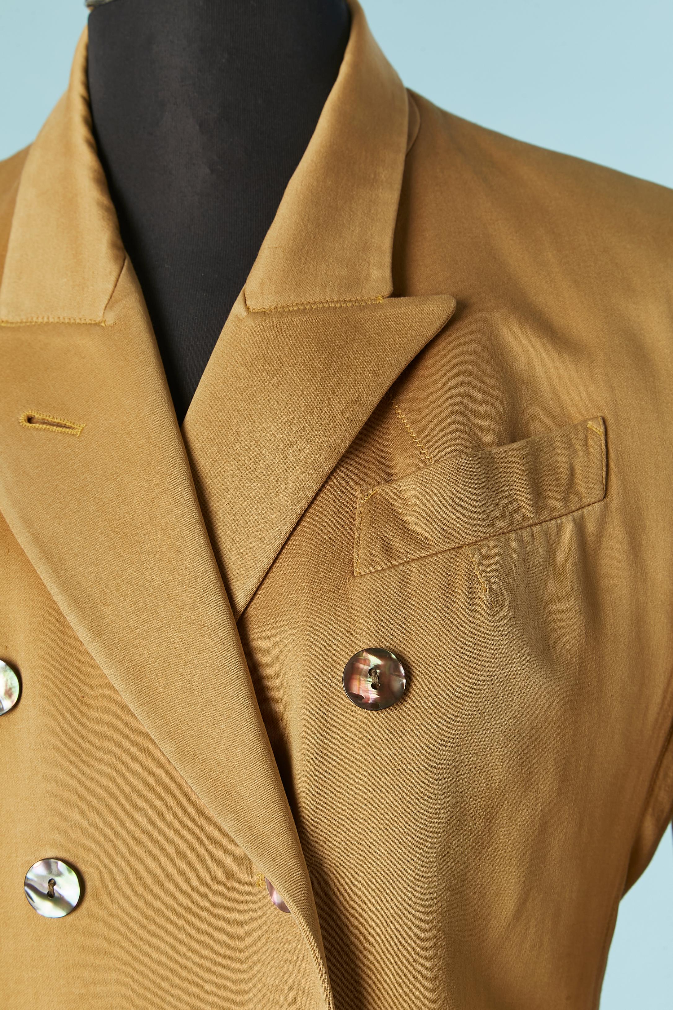 Zweireihiger Blazer aus Baumwolle. Schulterpolster. Innenfutter aus demselben Stoff an Schulter und Ärmel. Knopfverschluss aus Muschelschalen auf der Vorderseite und an den Manschetten.  Beidseitige Taschen mit Patte und eine Innentasche mit Knopf