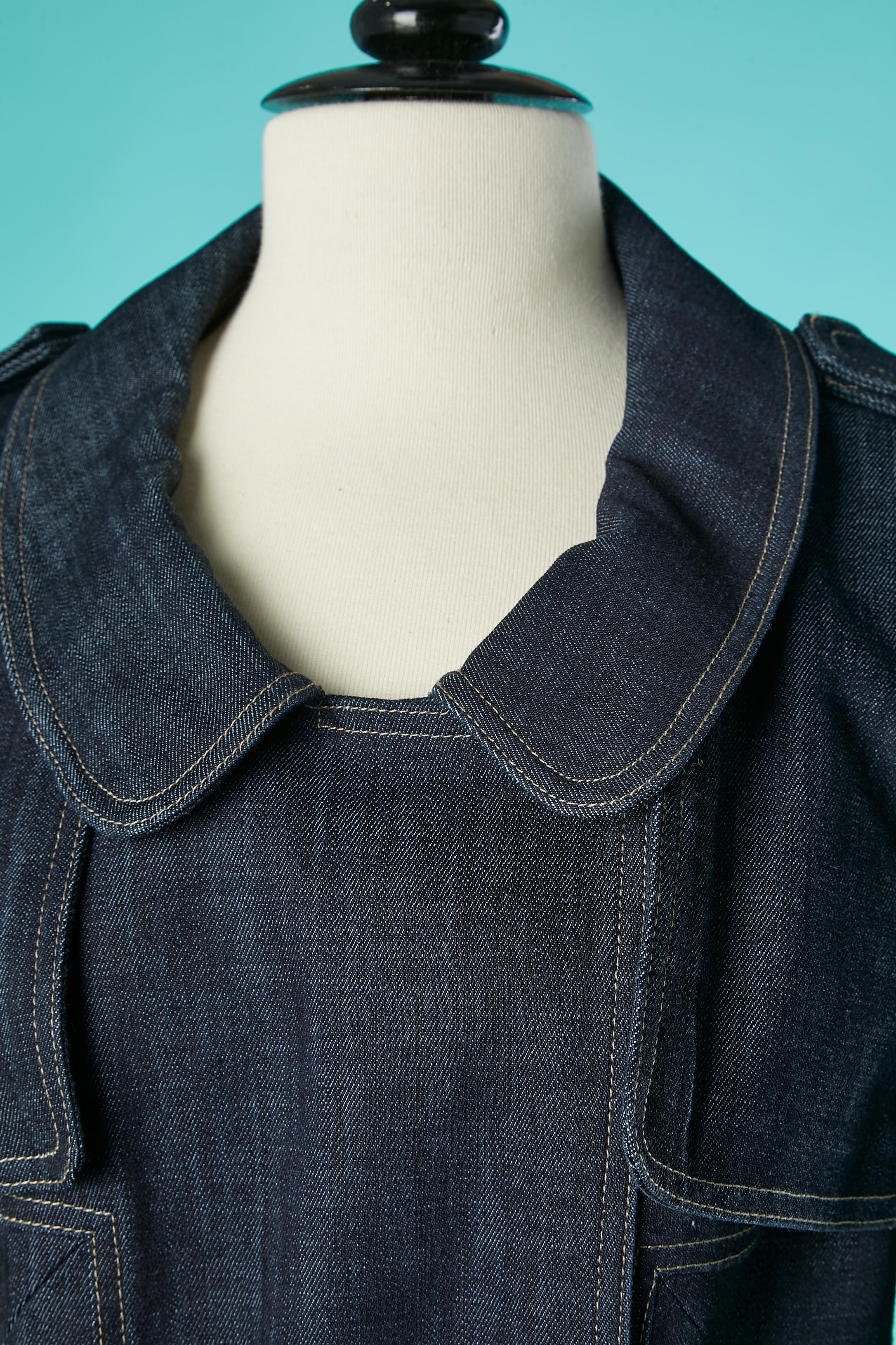 Zweireihige Jeansjacke im Trenchcoat-Stil. Zusammensetzung des Hauptgewebes: 74% Baumwolle, 25% Polyester, 1% Lycra. Baumwollfutter und Innenpaspel. Raglanärmel und offen an der Achselhöhle. Tasche, Gürtel und Gürtelschlaufe. Druckknopfverschluss.