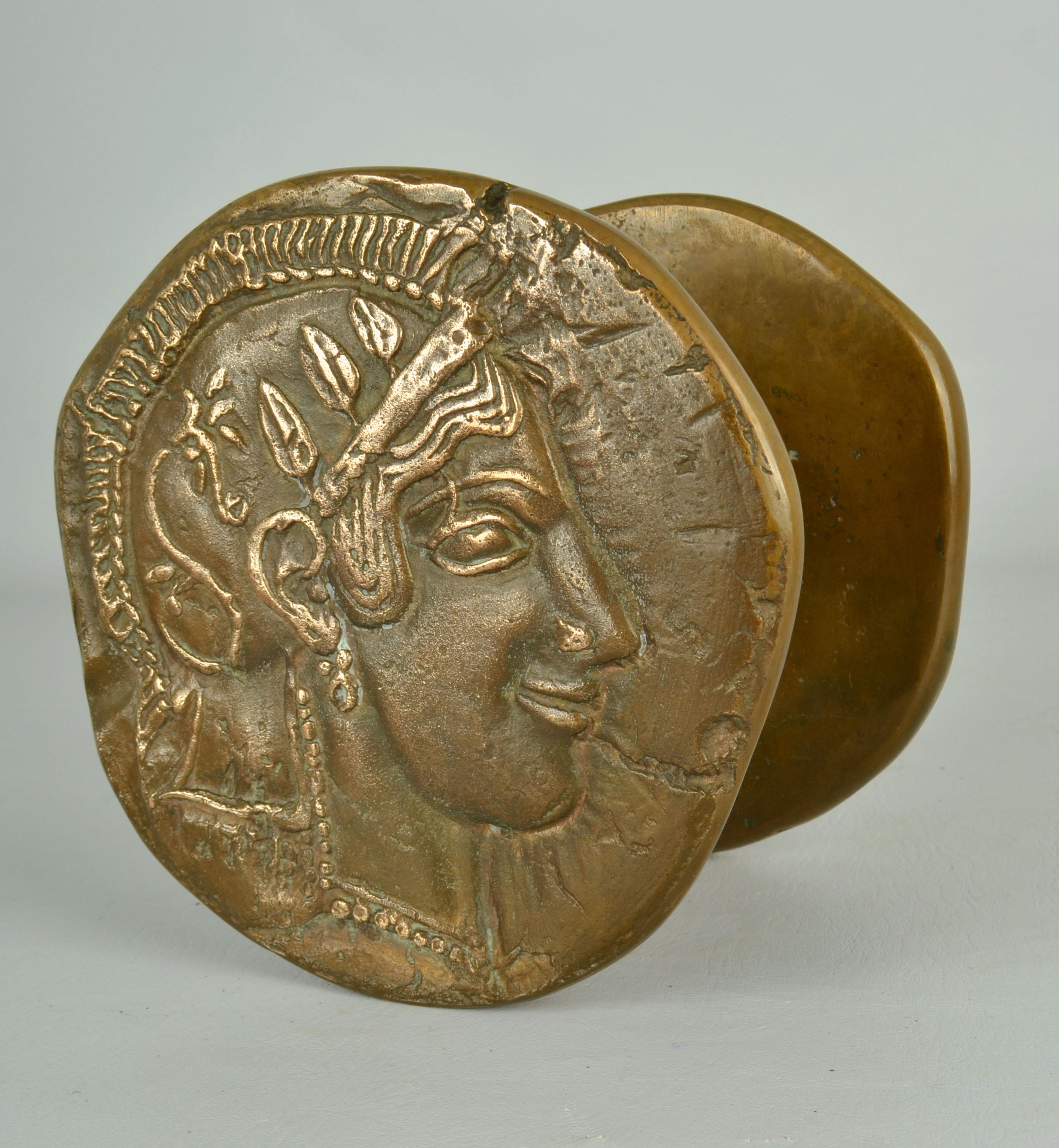 Zwei runde Bronzetürklinken nach antiken griechischen Münzen aus dem 5. Jh. v. Chr., die wahrscheinlich dem behelmten Kopf der Athene mit frontalem Auge und geflügeltem athenischem Helm ähneln. Die in Athen geprägten Münzen gehörten zu den