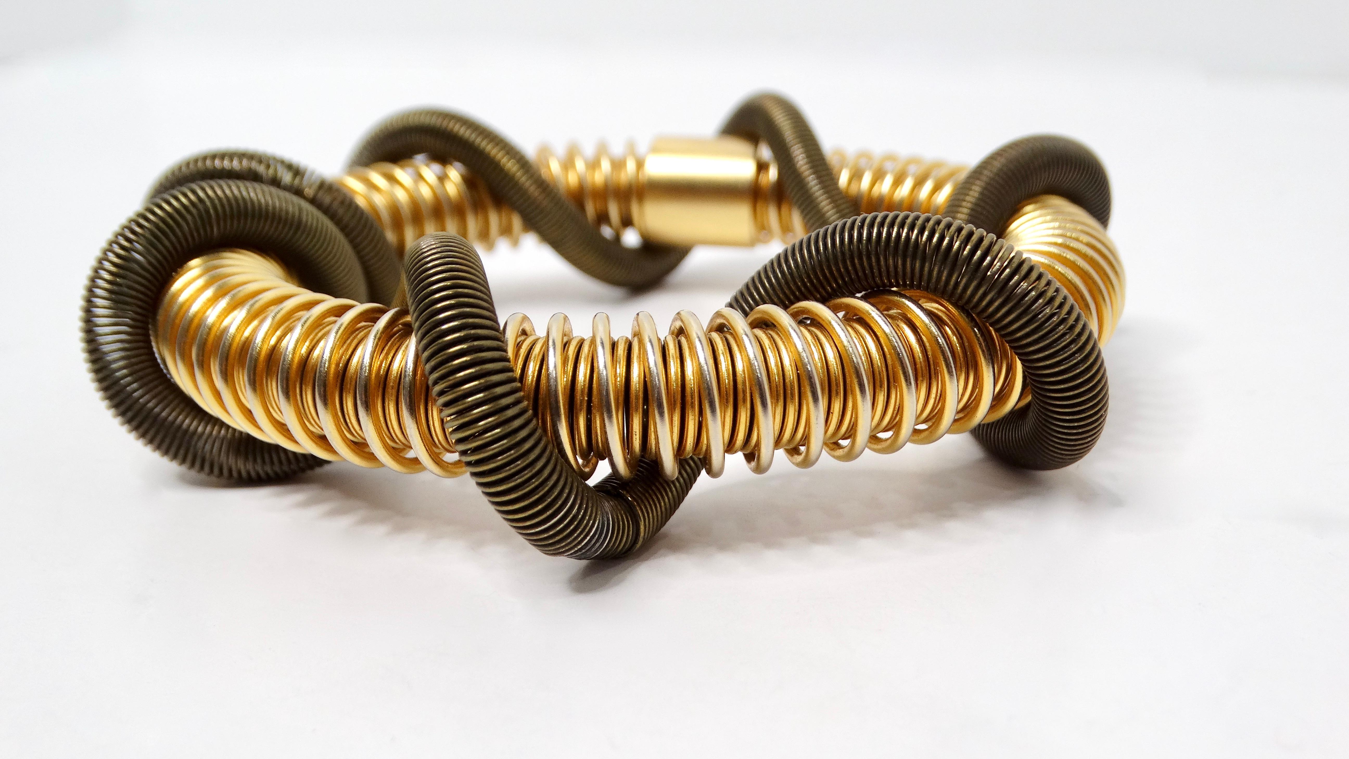 Eleganza moderna con il bracciale a filo geometrico Double Coil Green & Gold-Tone. Questo pezzo unico presenta un design innovativo, con uno splendido filo arrotolato in tonalità oro che circonda una bobina verde vibrante, creando un sorprendente