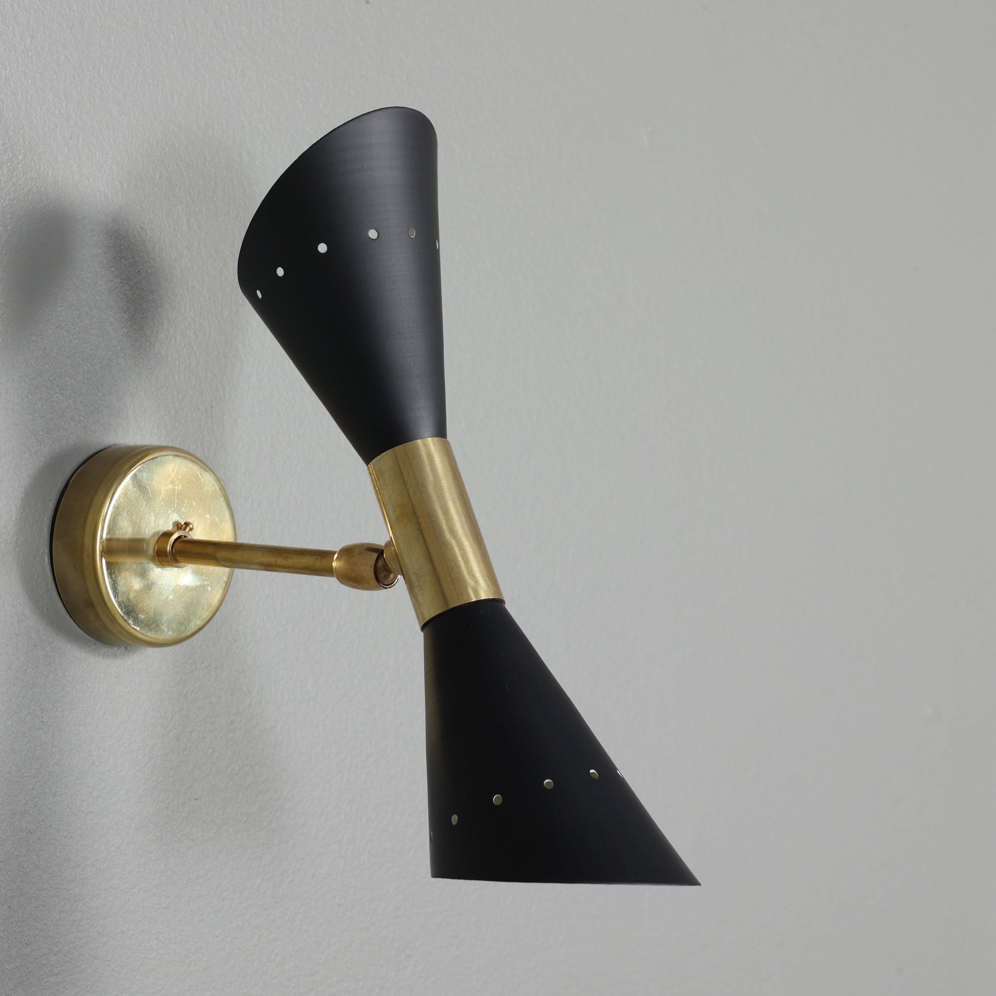A sculptural mid-century wall-mounted light fixture, featuring a refined interplay of polished or patinated brass and ivory lacquered metal. The sconce is designed with a double-cone shade and dual light sources, offering both ambient and
