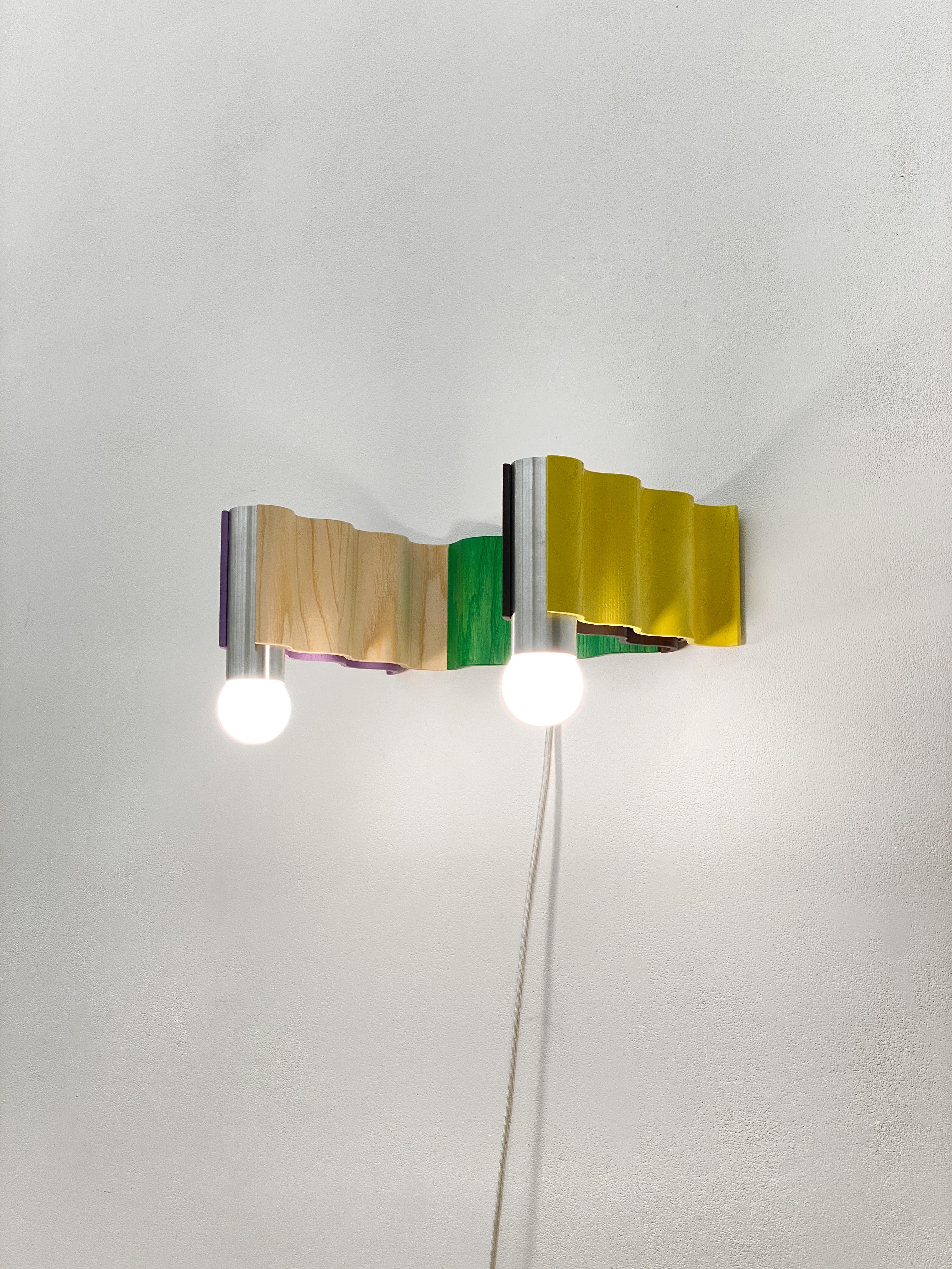 Multi-colored double sconce made from ash veneered plywood (painted purple, clear coated, stained green, brown painted, yellow painted) and brushed aluminium tubes. Designed for Fels's exhibition 