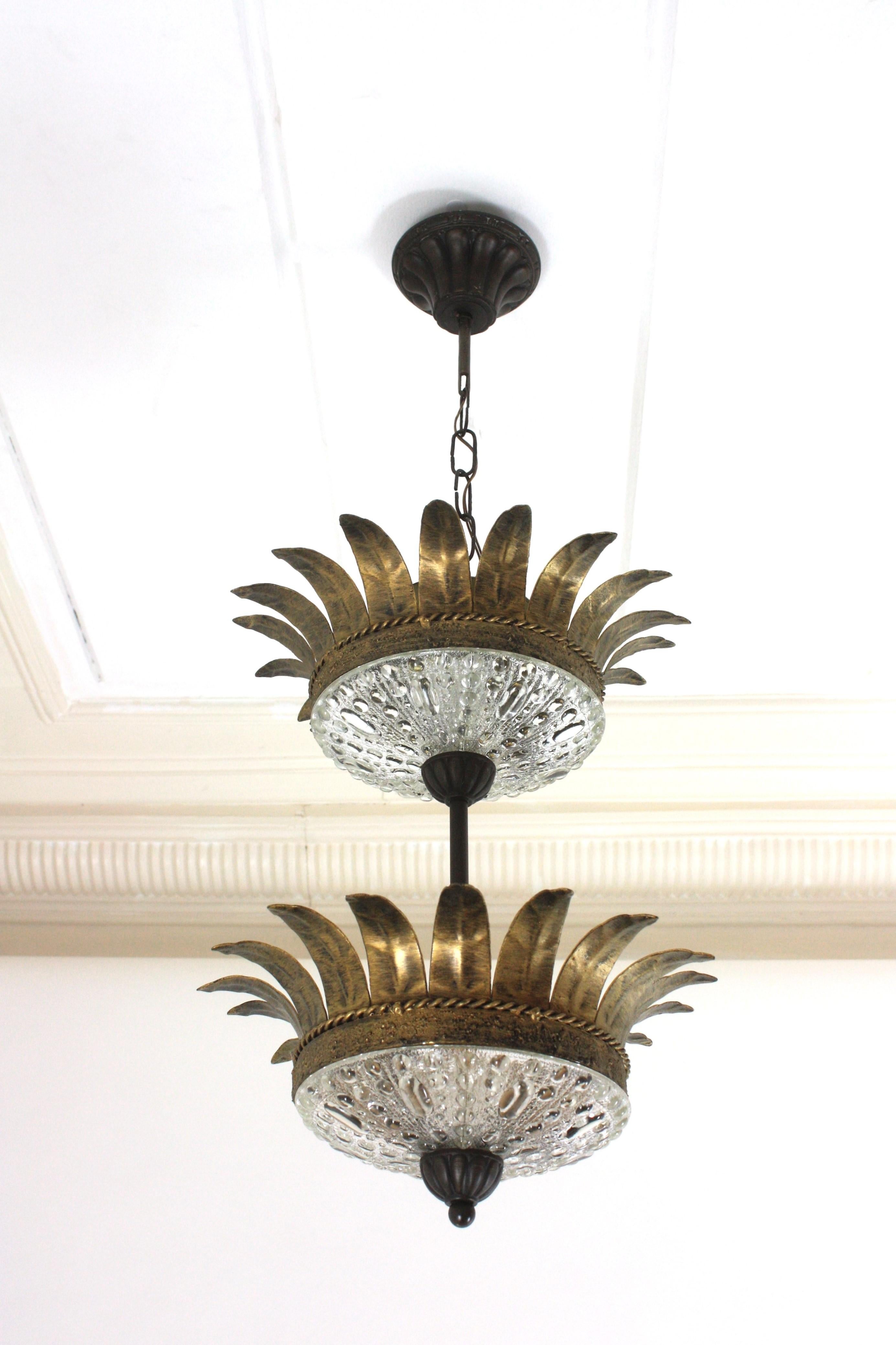 One of a kind neoclassical style sunburst two level crown chandelier from the Mid-Century Modern period, Spain, 1950s.
Rare find.
This ceiling suspension / pendant lamp features two sunburst crown shaped gilt light fixtures hanging joined between