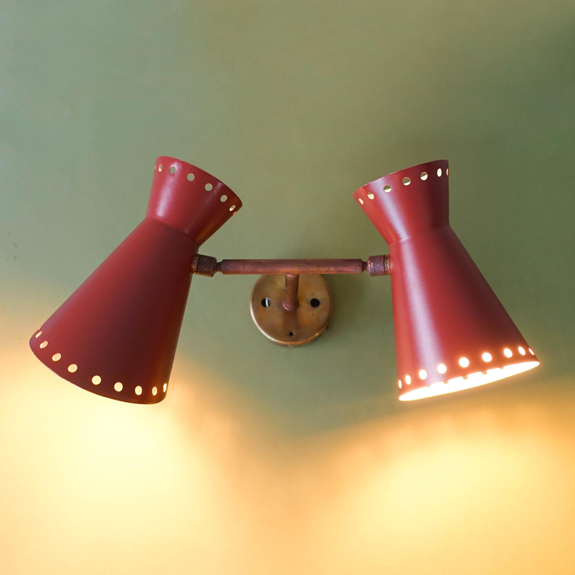 This two shade diabolo wall lamp was designed and produced in France during the 1950's. It has two metal shades, in brown perforated on top and down to spread the light. Each cone mounts one bulb. The three lampshades are attached to a brass arm