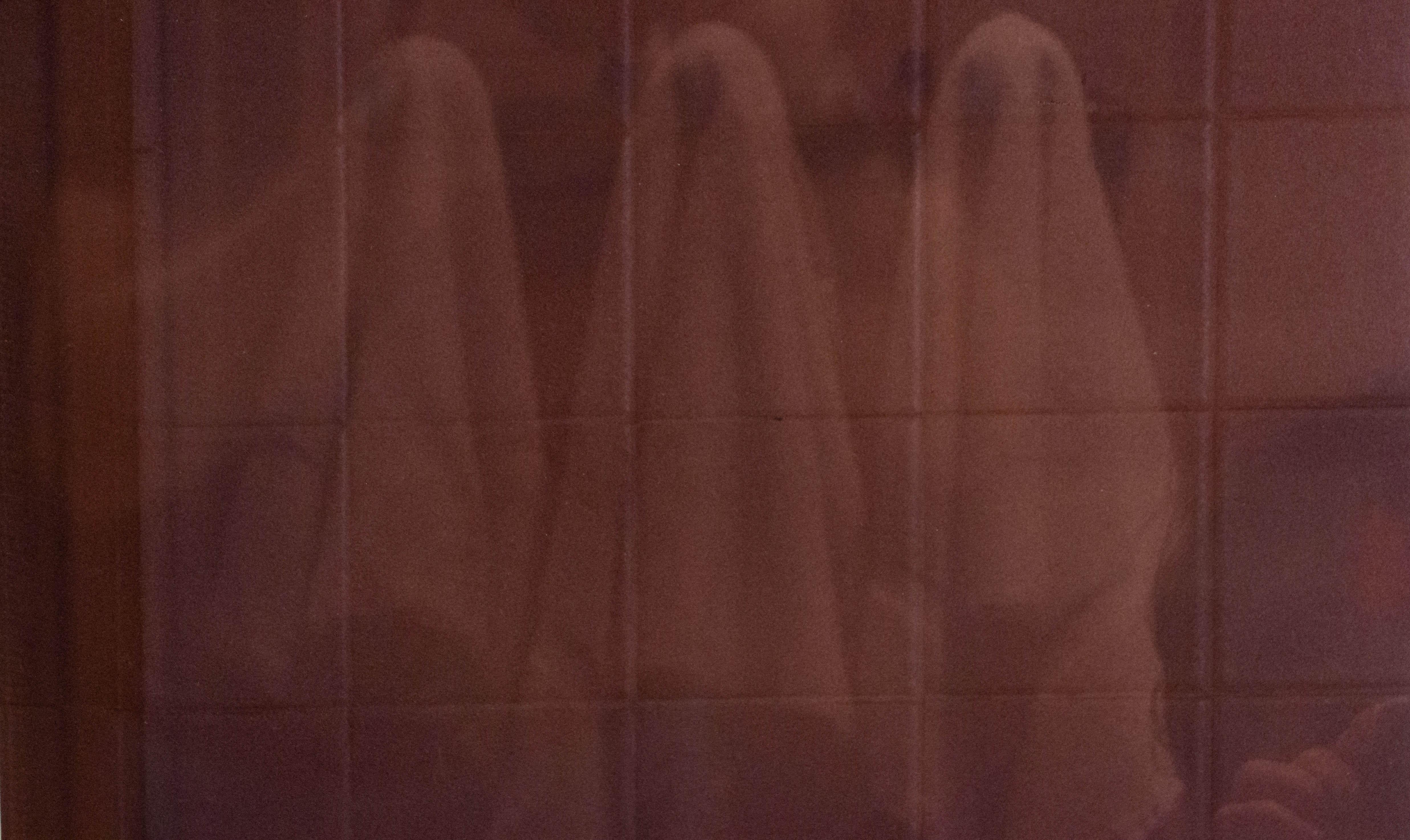 Double exposure color photograph of a person in a bathroom with a line of towels with a black frame and a white matte. Photograph by Shelley Harrison.
 