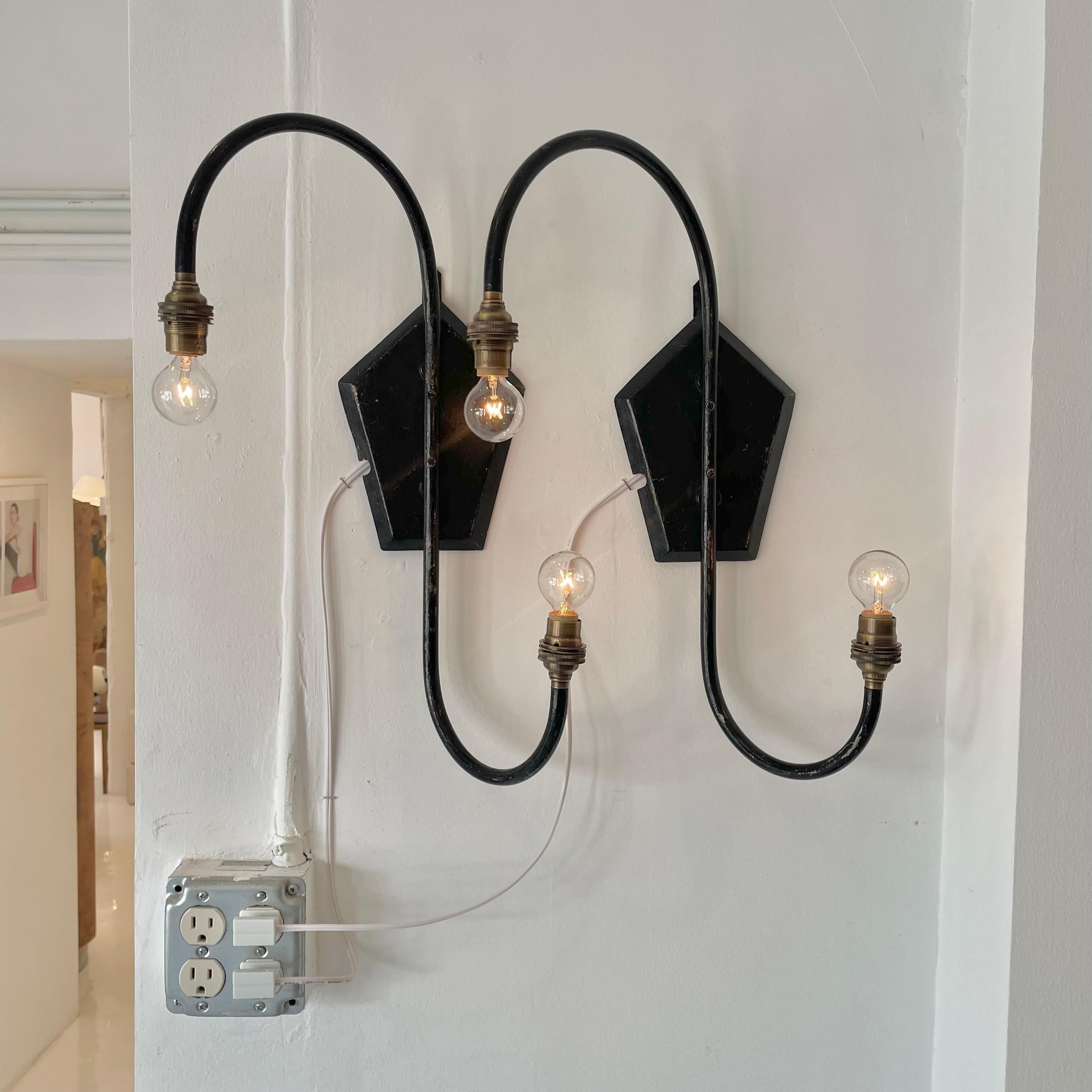Unique pair of mid century French sconces in the shape of two offset fish hooks. Metal tube body with a metal backplate hand painted in a gothic black paint with amazing patina. Eye catching lines with the option of custom mini shades for an
