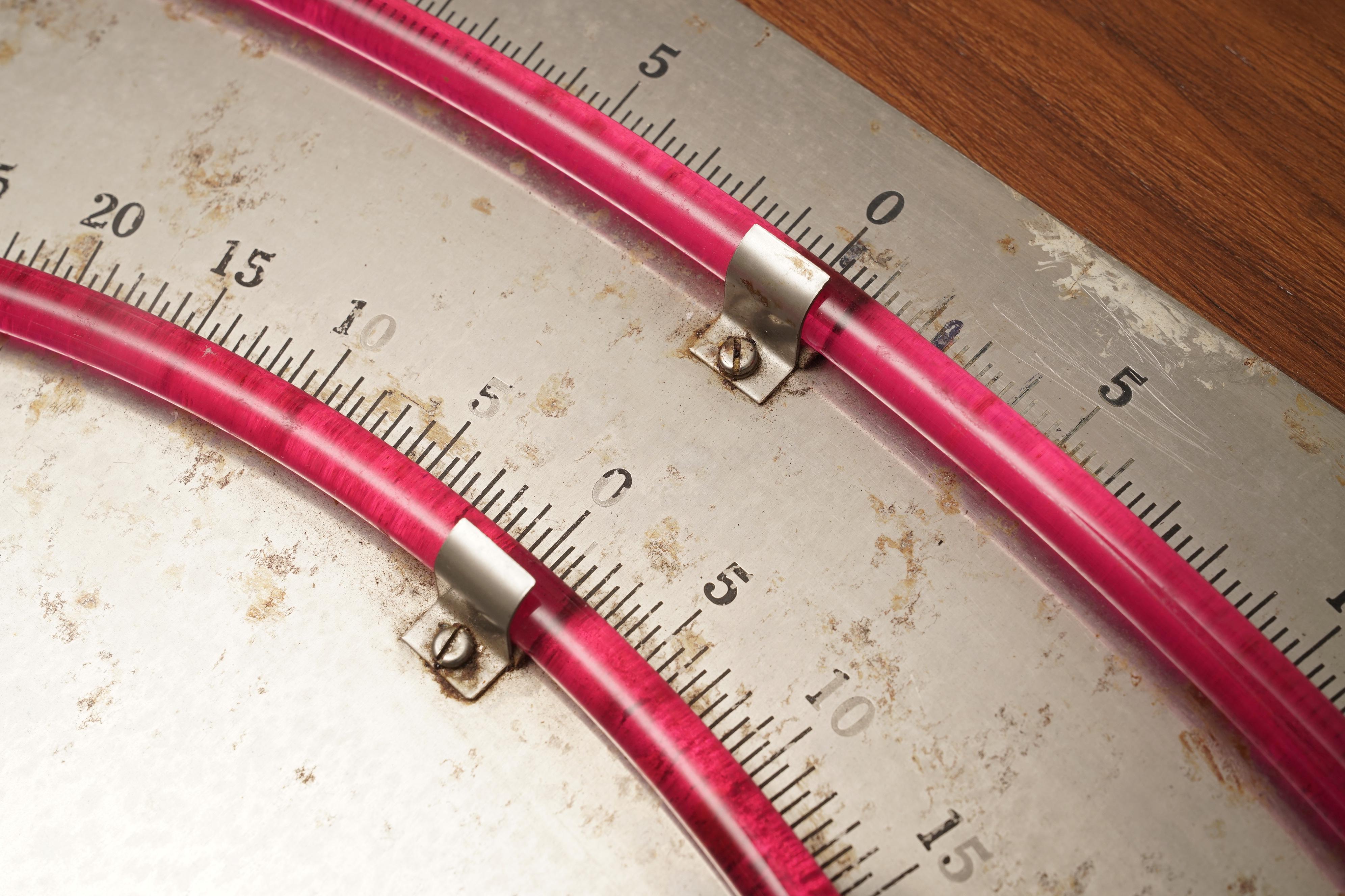 A double gauge bubble clinometer with precision glass tubing and nickel face mounted on a teak back plate. These tilt gauges were used on vessels to measure the angular slant of the ship. The readings are important when heeling underway, and also