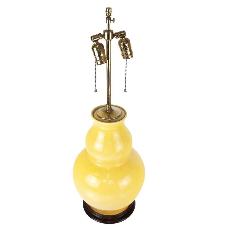A large, double gourd, Chinese glazed ceramic, yellow, vintage table lamp that sits on a round wood base. The lamp is designed with two sockets that operate on individual chain pull cords. This single yellow lamp brings sunshine and light to the