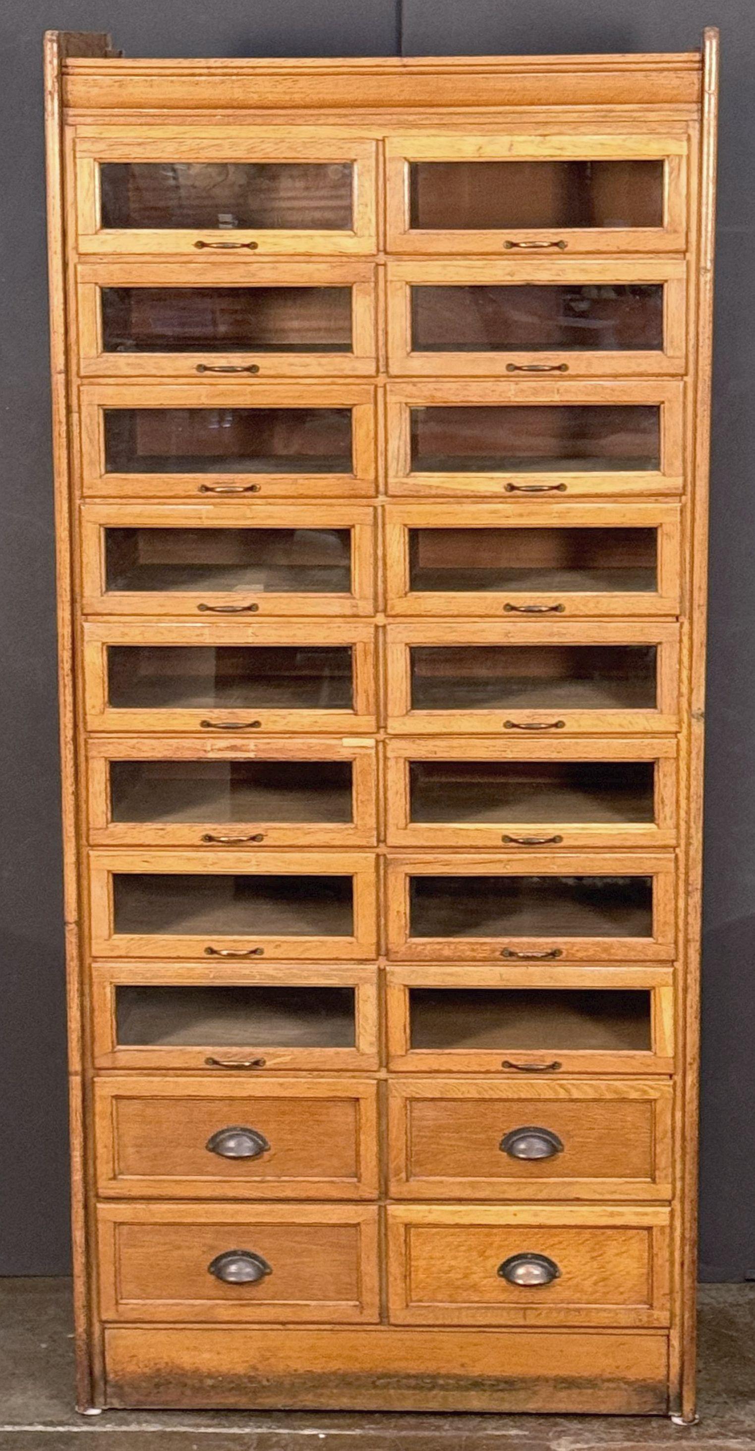 Ein hübscher doppelter Kurzwarenschrank aus patinierter Eiche mit getäfelten Seiten aus England mit:

(16) Schubladen mit Glasfront über vier schrankartigen Schubladen - (20) Schubladen insgesamt.

Die Schubladen sind mit Metallgriffen ausgestattet