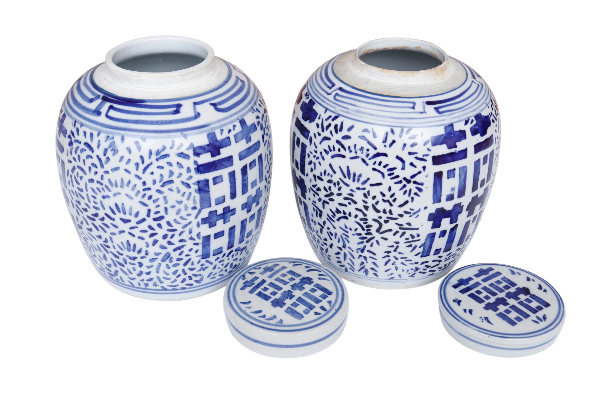 A pair of blue and white Chinese ceramic ginger jars with matching lids. Hand painted with the double happiness symbol framed with a floral motif in bold cobalt blue. Marked underneath “Made in China” in English and Hanzi. Dimensions per jar.