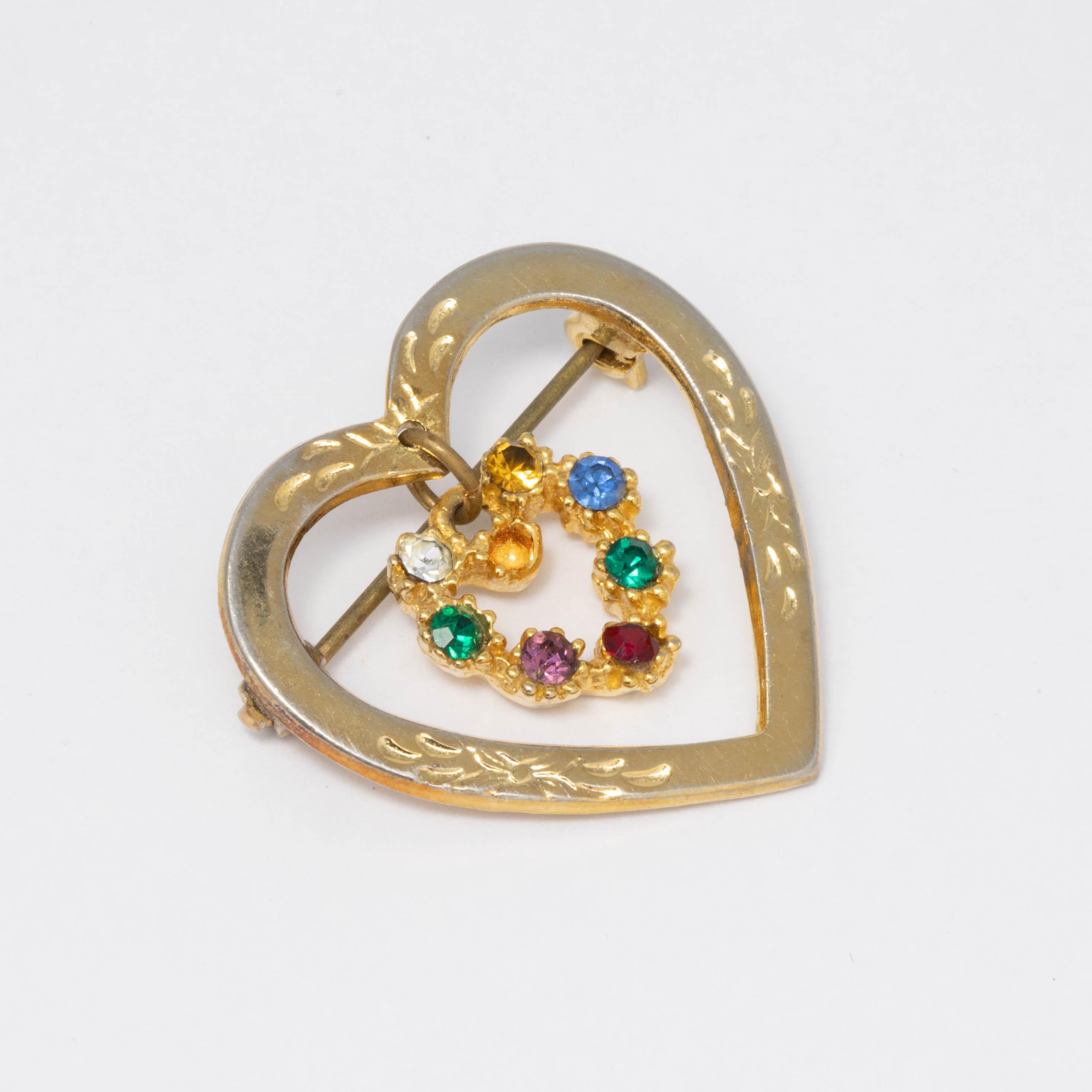An accented gold tone open-center heart, with a second crystal-encrusted heart dangling inside. 

Mid 1900s pin brooch.