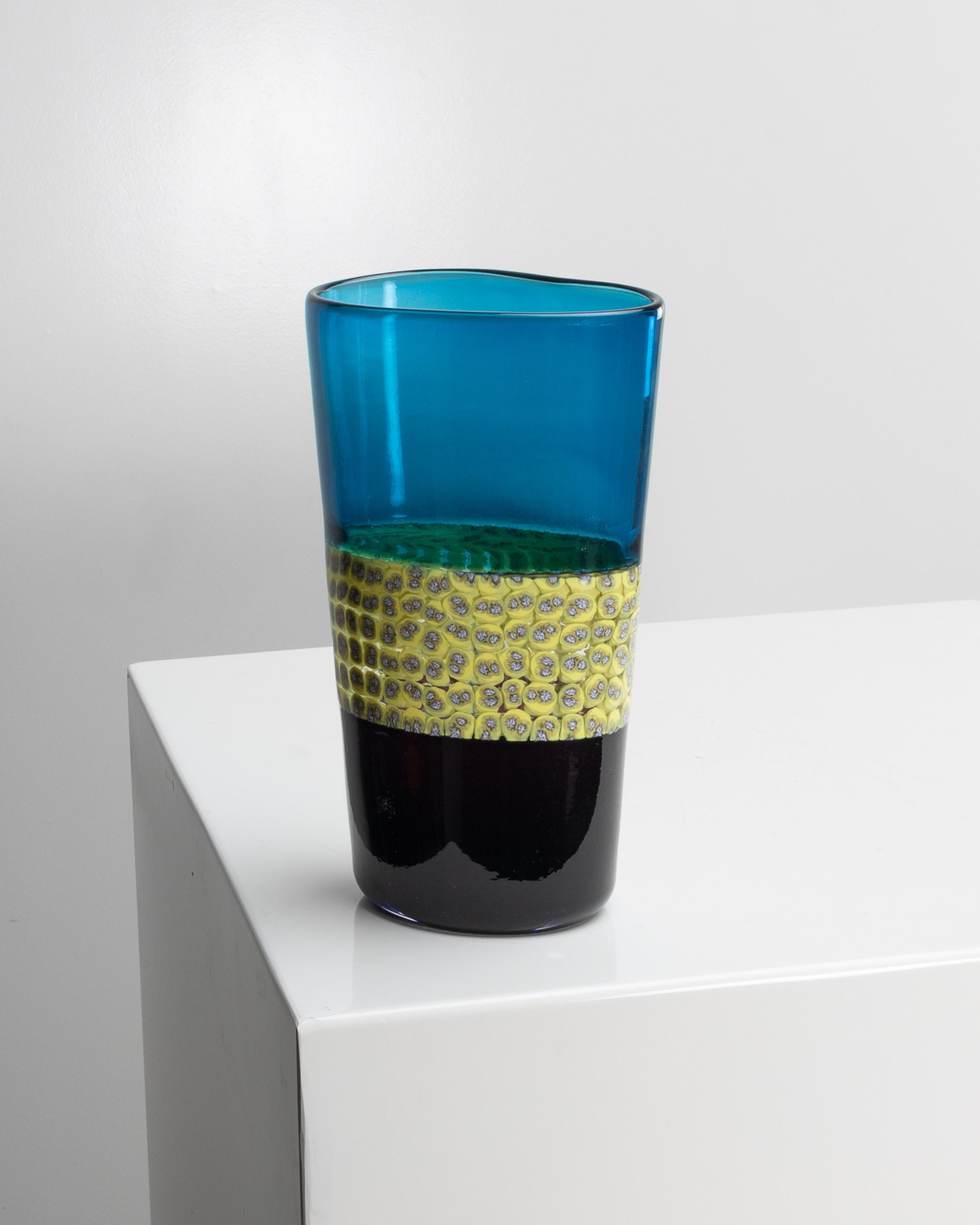 Doppio incalmo e murrina Riccardo Licata - Vaso in vetro soffiato - Venini Murano.
Vaso a sezione irregolare appiattita in vetro trasparente doppio incalmo melanzana e azzurro.
Fascia centrale in vetro trasparente decorata con murrine di colore