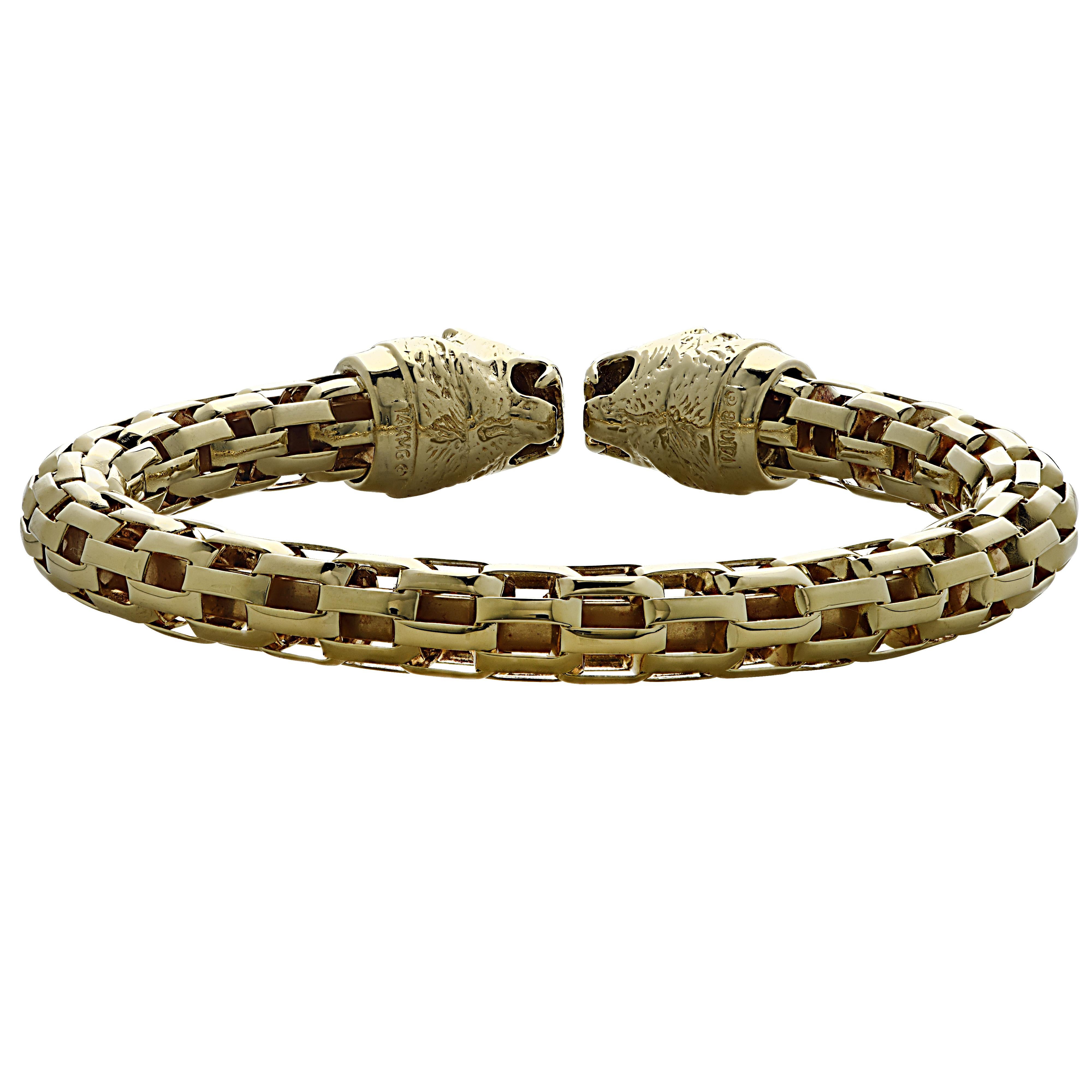 Double Lion head cuff bangle bracelet crafted in yellow gold and steel. Two lion heads, detailed with sapphire eyes, face-off in this stunning tubular cuff bangle bracelet. The bracelet has an inner diameter of 2.25 inches by  2.1 inches, and
