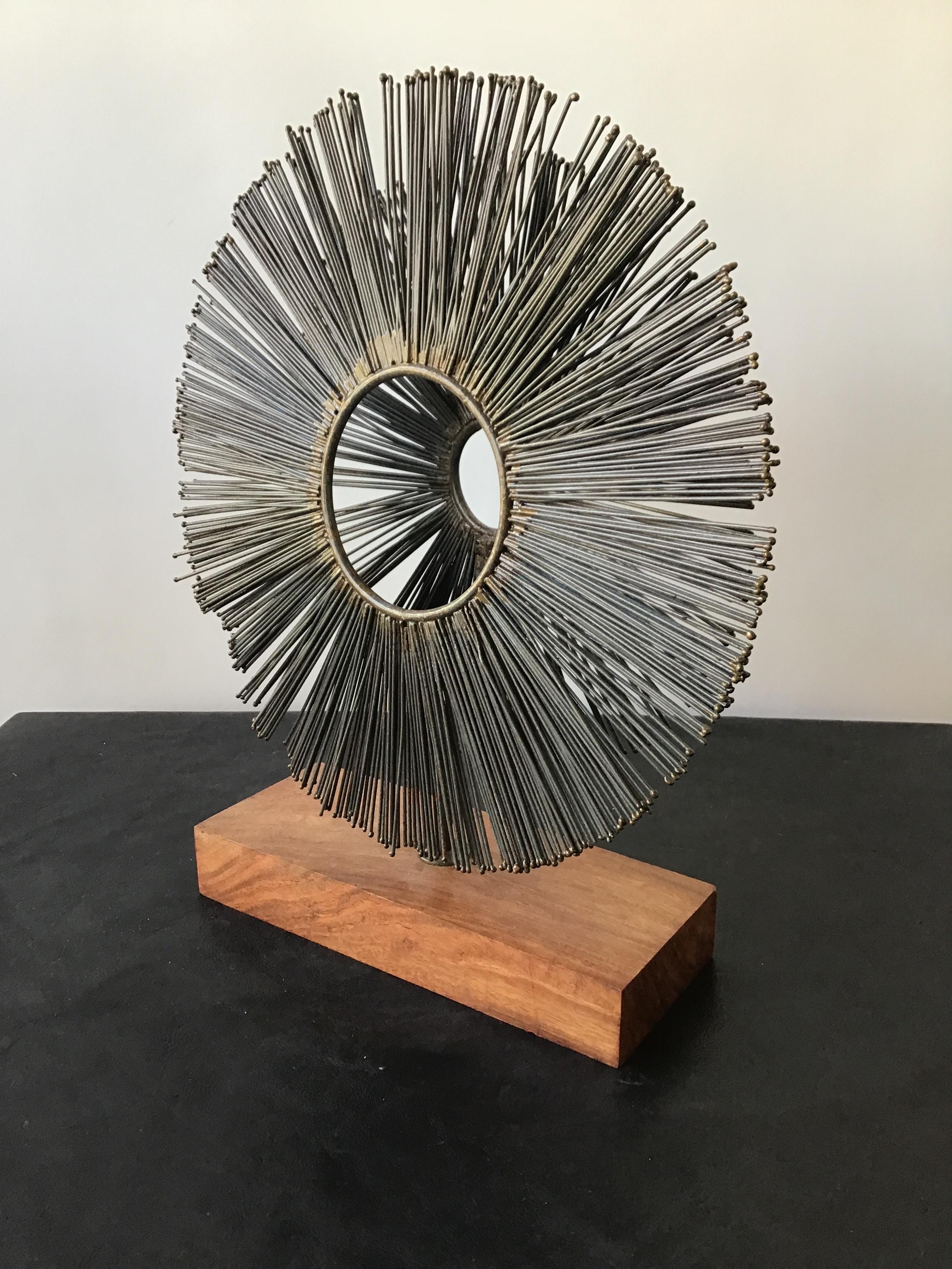 Double metal sunburst sculpture on wood base.