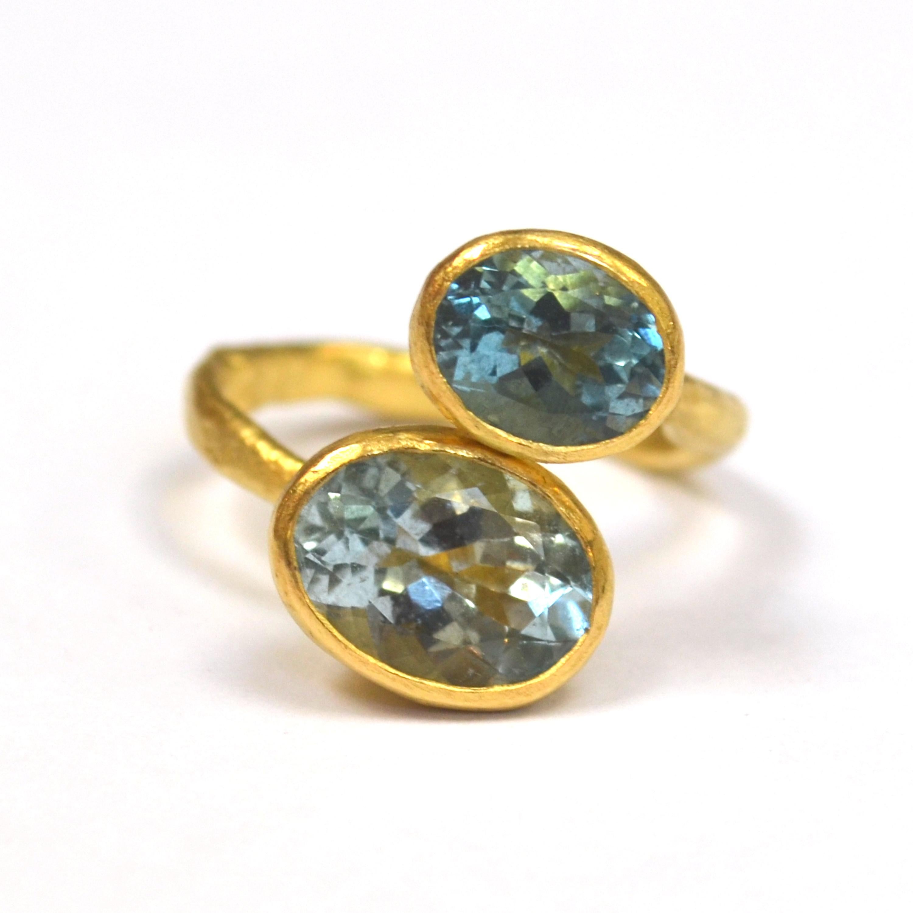 18k Gold organic textured handmade open ring. With two oval Aquamarines, 4 carats and 2 carats each. Each one has a slightly different tone of blue, one is bright and watery, the other a slightly darker blue, both with beautiful facets that create