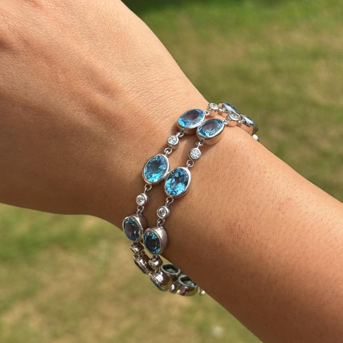 Questo braccialetto tennis a doppia fila di topazi blu e zirconi è un braccialetto tennis a doppia fila realizzato in luminoso argento 925. Con una squisita disposizione di gemme di topazio azzurro dal taglio ovale intervallate da brillanti zirconi