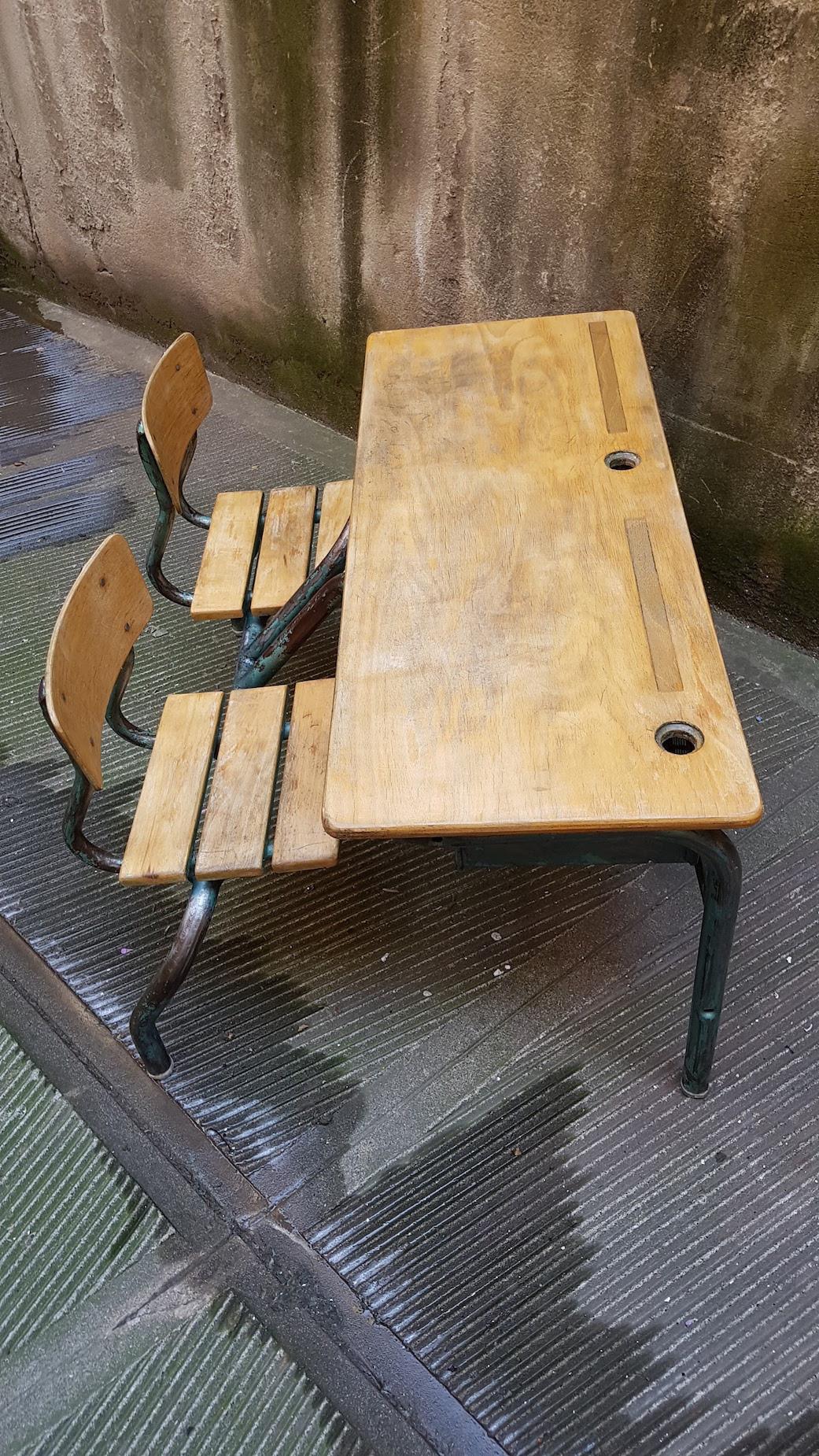 This charming double bench from the 1950s has its structure made by iron and wooden table and seats. It is in excellent condition with the original 2 inkcups and the shelves for books under the table. It could be an amazing alternative to a desk for