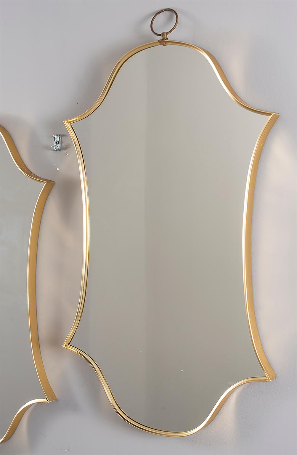 Pair of midcentury circa 1970s brass framed mirrors have an elongated double shield form shape with a brass hanging loop at the top. Sold and priced as a pair.
  