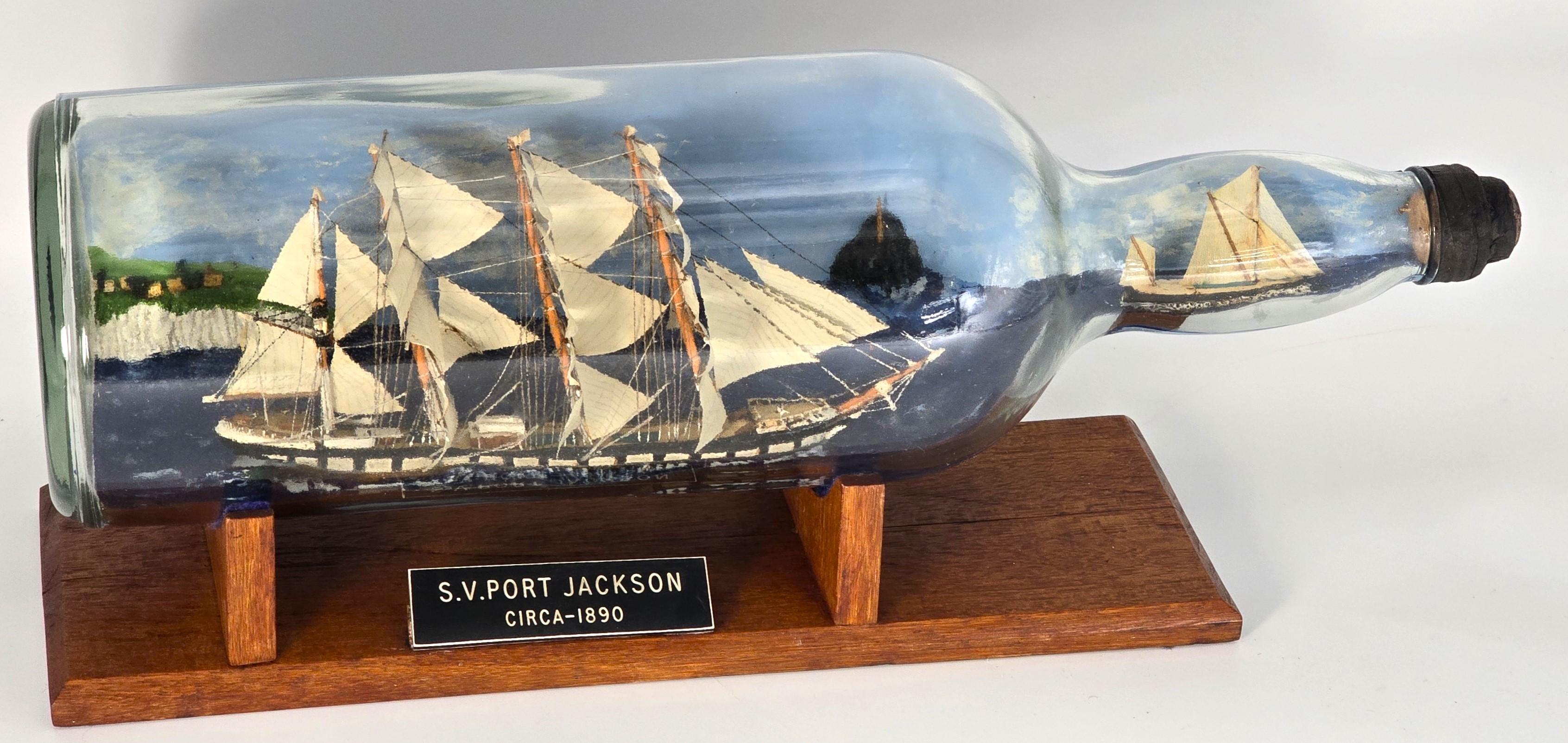 

This superb folk art diorama ship in a bottle has been wonderfully modelled and constructed in a very large Bells whiskey bottle. The type of bottle used for display in a pub or inn.
The main vessel is the Australian four mast iron ship, the SV