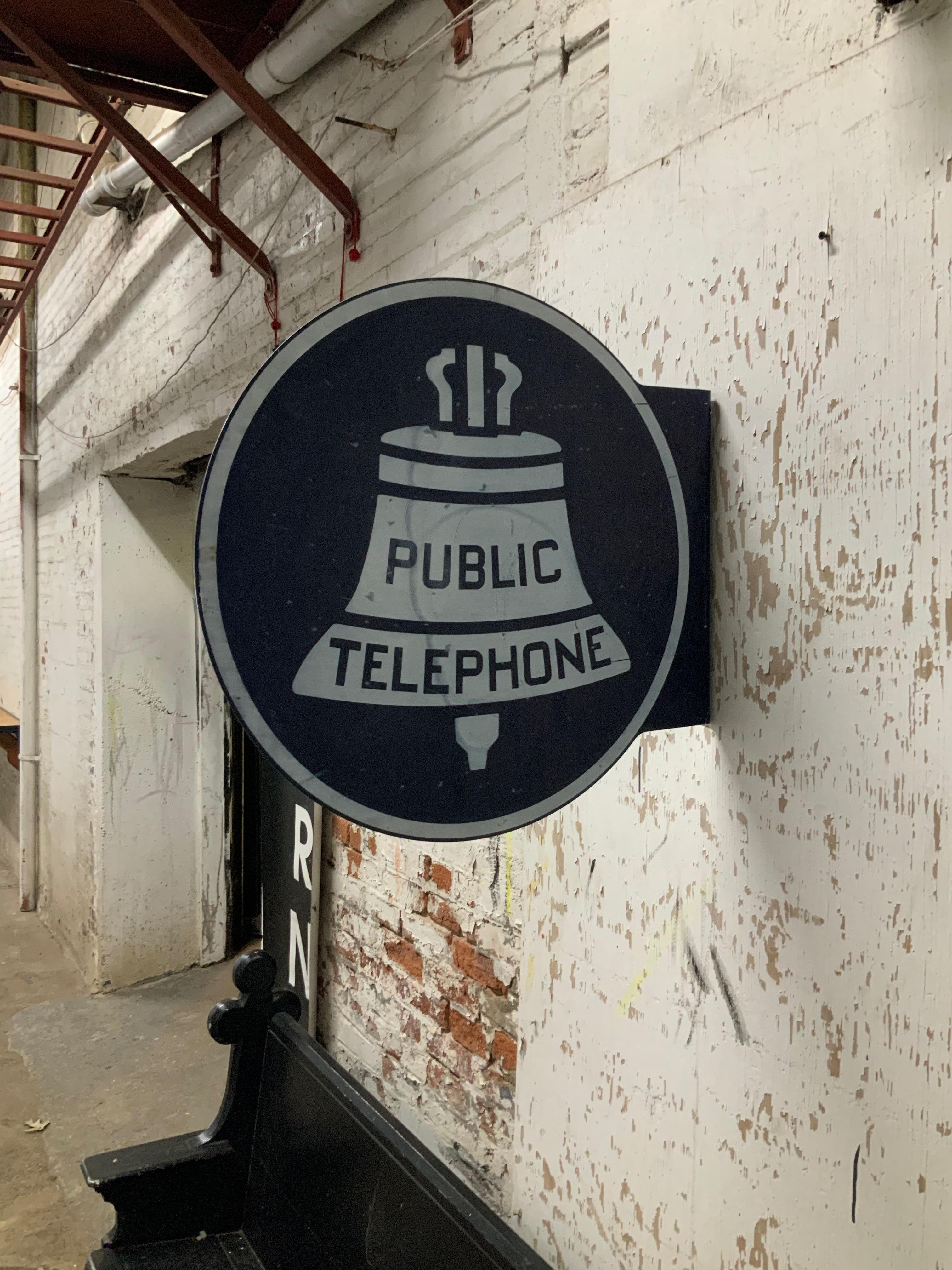 Porcelain enamel round Public Phone sign, circa 1940-1950. Round double side flanged sign with grommets that would attach the sign to a phone booth. Wear commensurate with age and exposure to the elements. Some light scratches and