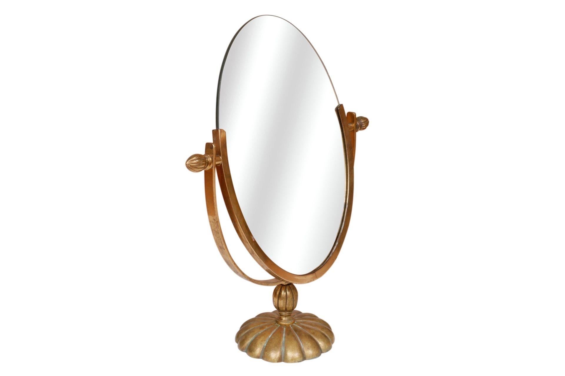 A traditional double sided oval vanity mirror in brass. The mirror can be adjusted with reeded acorn finial hinges at each side. The base is a large rosette with a scalloped edge.