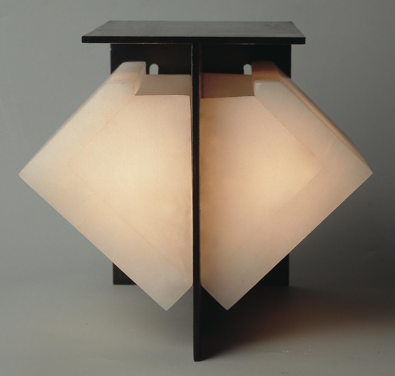 Designed in 1923, the rigorous geometry and single volume of this wall lamp reveal the mineral nature of alabaster and Pierre Chareau's minimalist choice, enhanced by the black metal / white alabaster contrast.