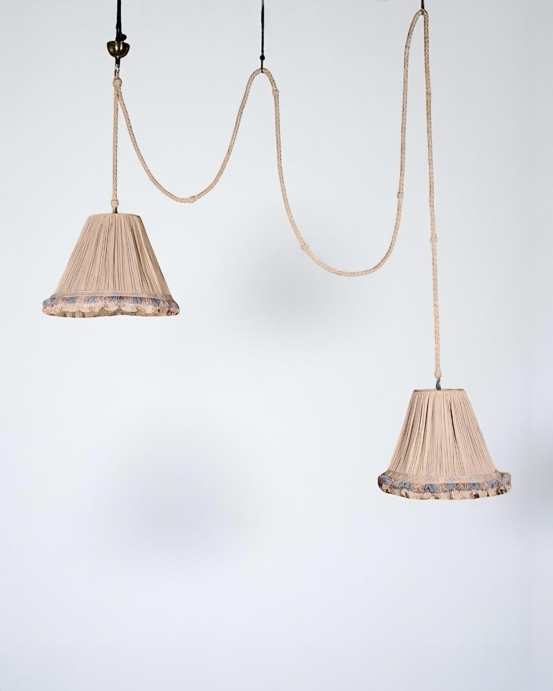 Double silk, rope and brass draped pendant, by Cenacchi, made in Molinella, Italy, 1960s.
Romantic and refined, this double pendant light features two silk-draped lampshades trimmed with elegant blue, pink, and mocha-brown passementerie. The two
