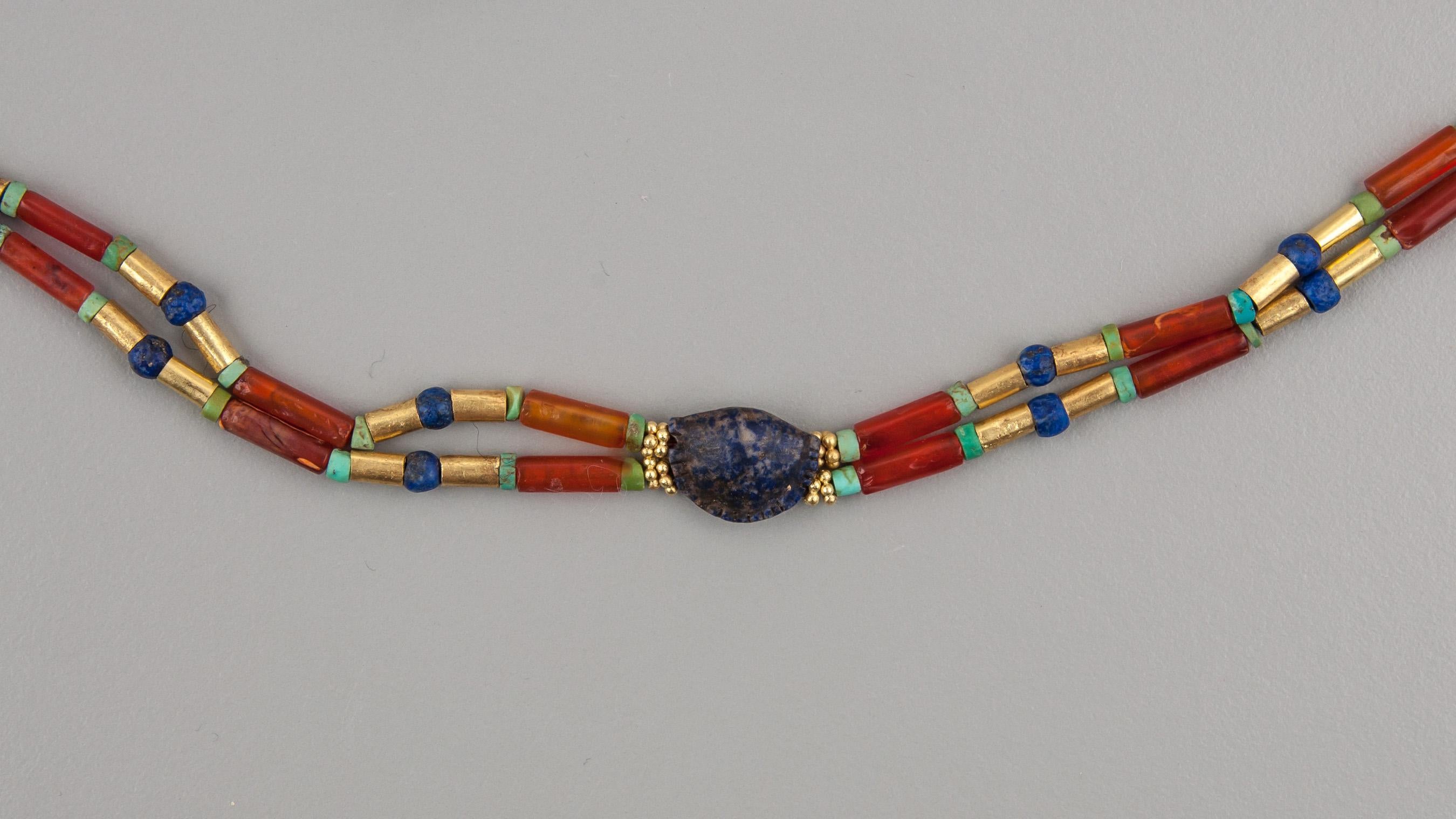 A double strand necklace of choker length of lapis lazuli, carnelian, turquoise and gold beads with a lapis lazuli cowrie shell bead in the center. The lapis shell is 1.5 cm in length, 1.14 cm in width and 5.9 mm in thickness at the top. The