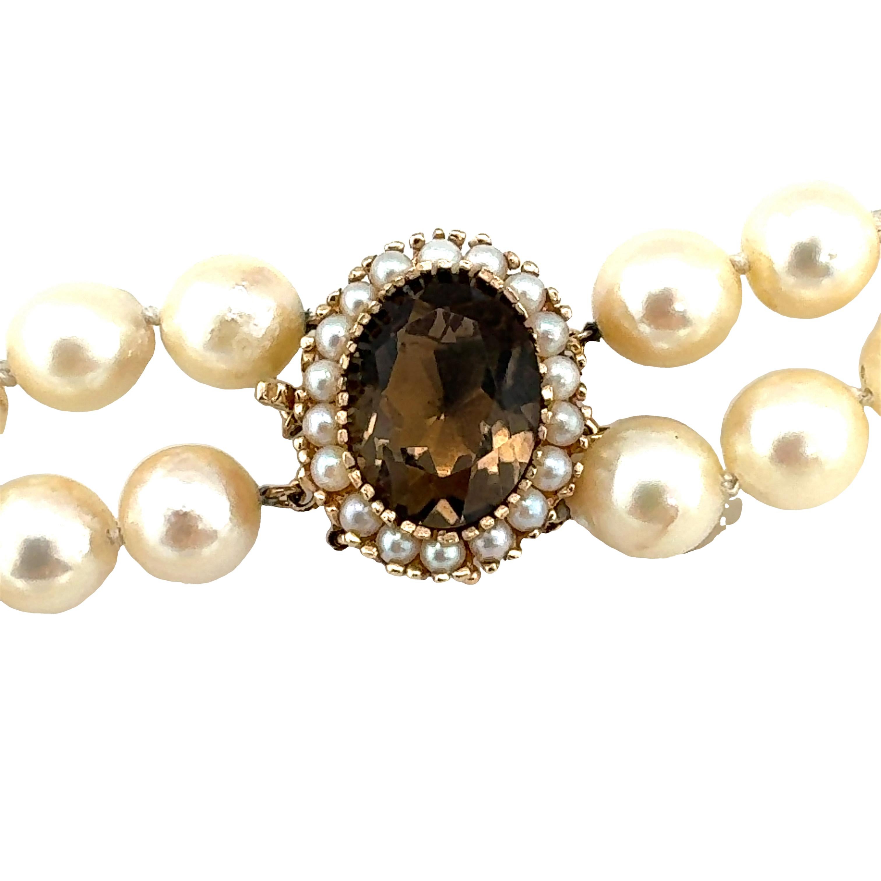 One double-strand pearl necklace featuring 116 round, cream color cultured pearls measuring 8.50-9.00 millimeters in diameter on average. 14K yellow gold clasp with an oval brilliant cut smoky quartz weighing approximately 6.67 ct. along with a seed