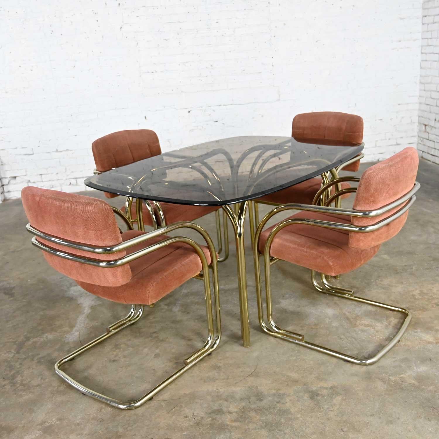 Beautiful set of four modern or Hollywood Regency double tube curved arm brass plate cantilever chairs with blush chenille upholstery and matching table with rounded rectangular or “stadium” shaped smoked glass top and double tube brass plated base