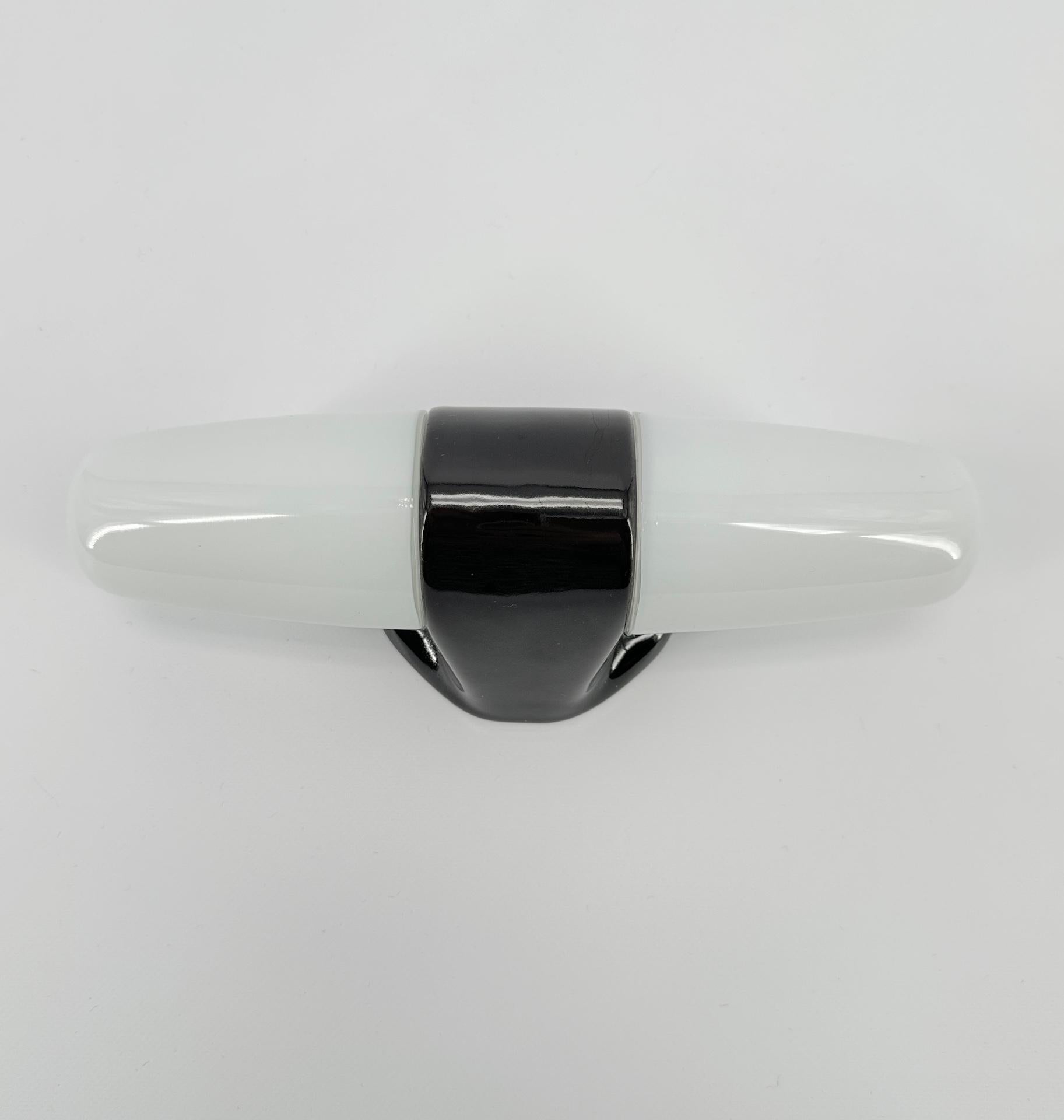 Cette applique en porcelaine blanche et abat-jour en verre opalin a été conçue par le designer allemand Wilhelm Wagenfeld, qui a étudié à l'école du Bauhaus.

Ce modèle date de 1958 et présente des lignes épurées, rondes et élégantes, un design