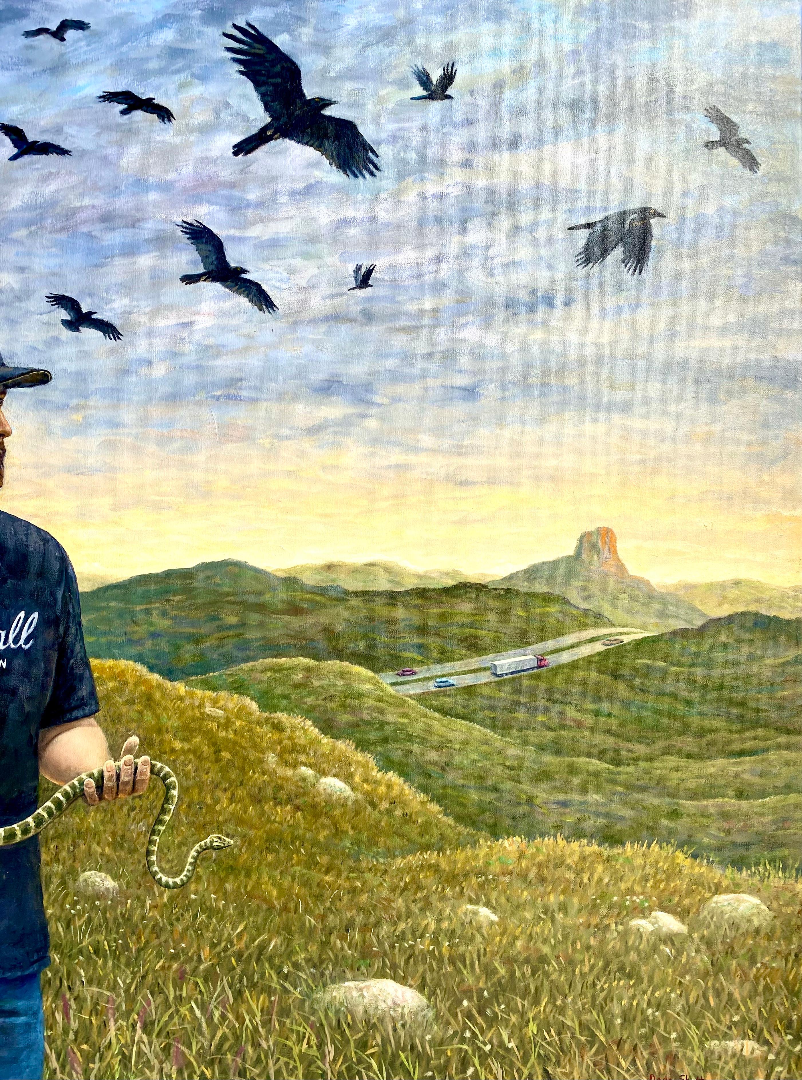 A man stands alone in a field wearing a black Marhsall Amplification shirt and a black hat. He's holding a snake with both hands while a flock of birds flys overhead. The Blue Bird Motel stands in the background, while a nearby highway can be seen