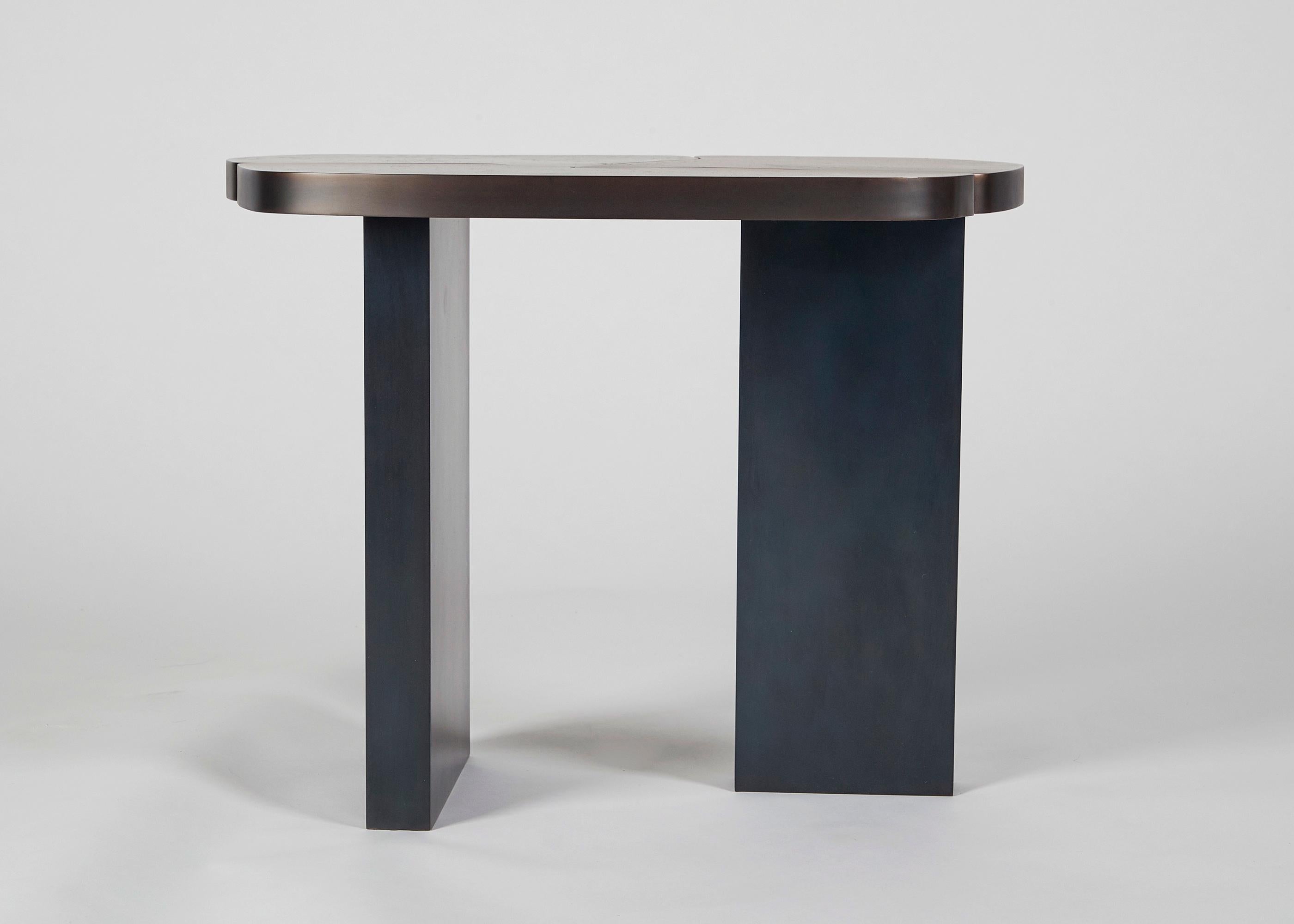 This table's amorphous, cast bronze top seems to be separating into three pieces as the earth upon a fault. It rests atop two rectangular, blackened steel legs, one wider than the other, which serve to support the piece with the stability of