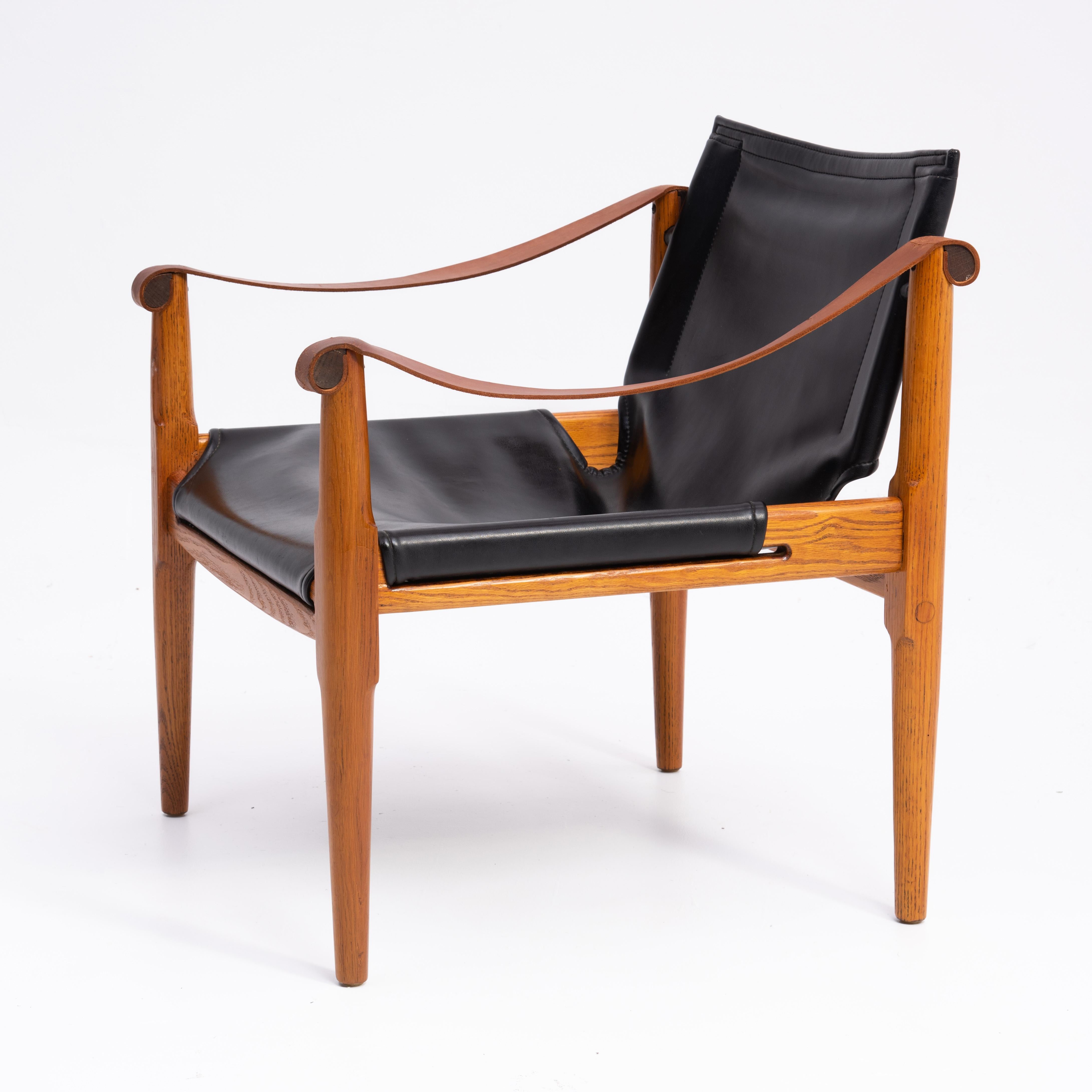 A vintage Mid-Century Modern brown Saltman safari chair designed by Douglas Heaslett. Solid oak frame with black vinyl seat and brown leather arms.