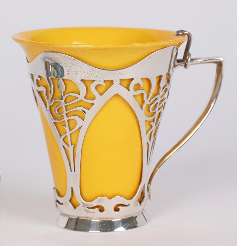 A scarce and exceptional Doulton Burslem Art Deco silver mounted coffee cup set complete with saucer and original spoon and dated 1929. The porcelain trumpet shaped coffee cup sits within a purpose made silver mount with stylized pierced panels with