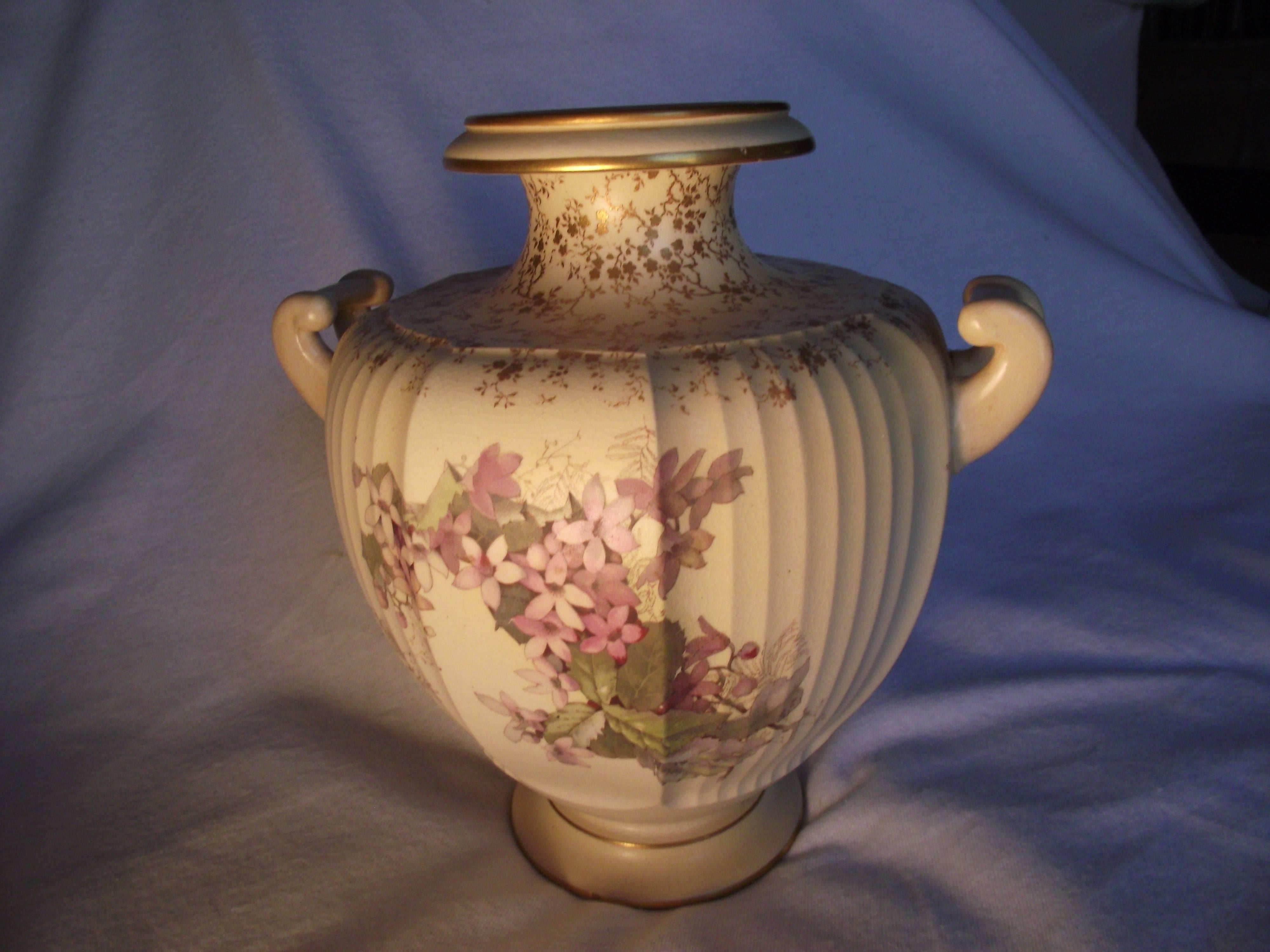 Charming warm colored vase with a hand-painted lilac and leaf pattern. The top and bottom have gold accents. No chips or cracks but there is age crackling in the glaze.

Sir Henry Doulton established and art studio in Burslem, Stoke-on-trent in