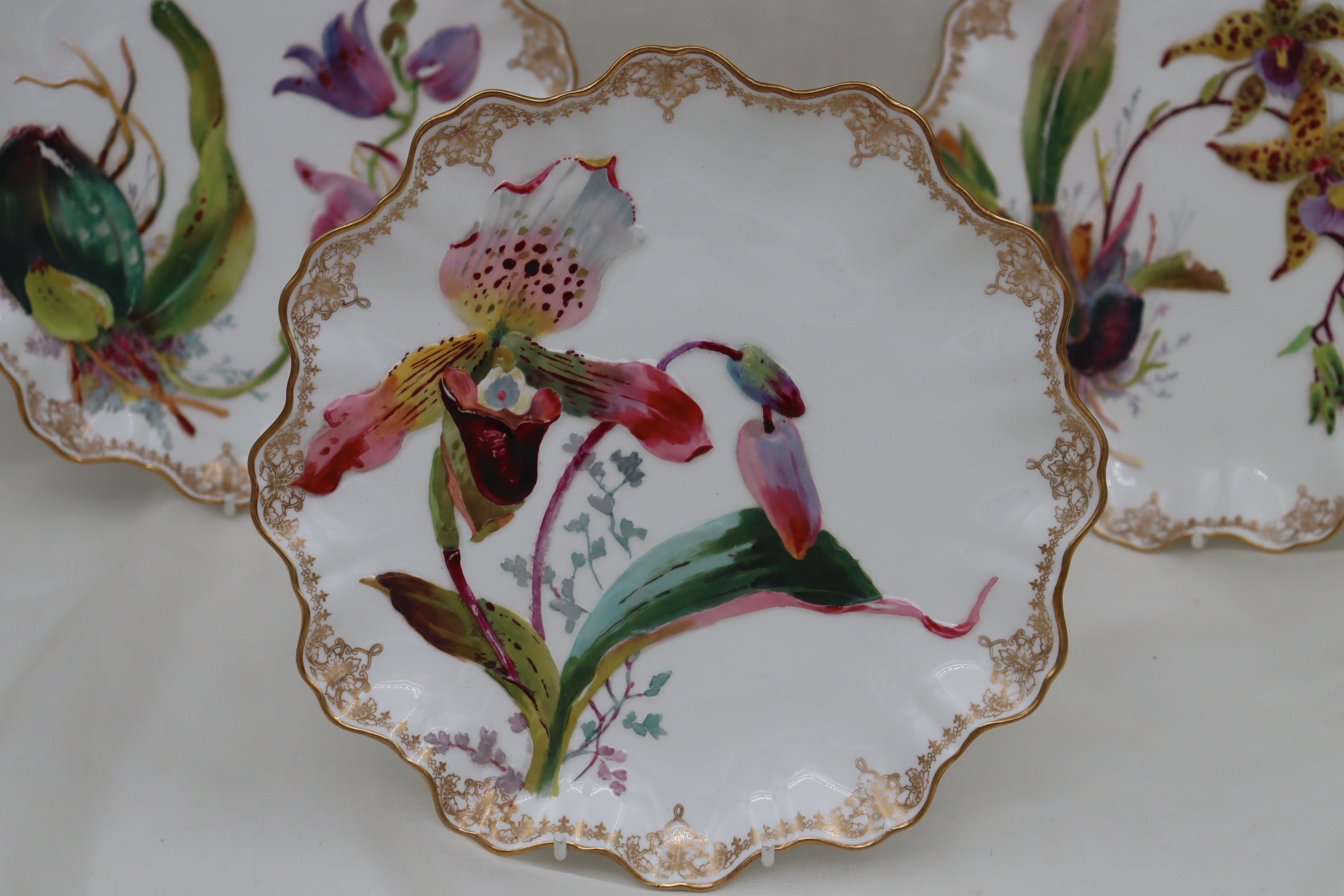 This Doulton Burslem part dessert set comprises six plates and a low comport. All pieces feature raised, moulded depictions of a variety of orchids which have been hand coloured and sit nicely against the white porcelain body. The scalloped rim has