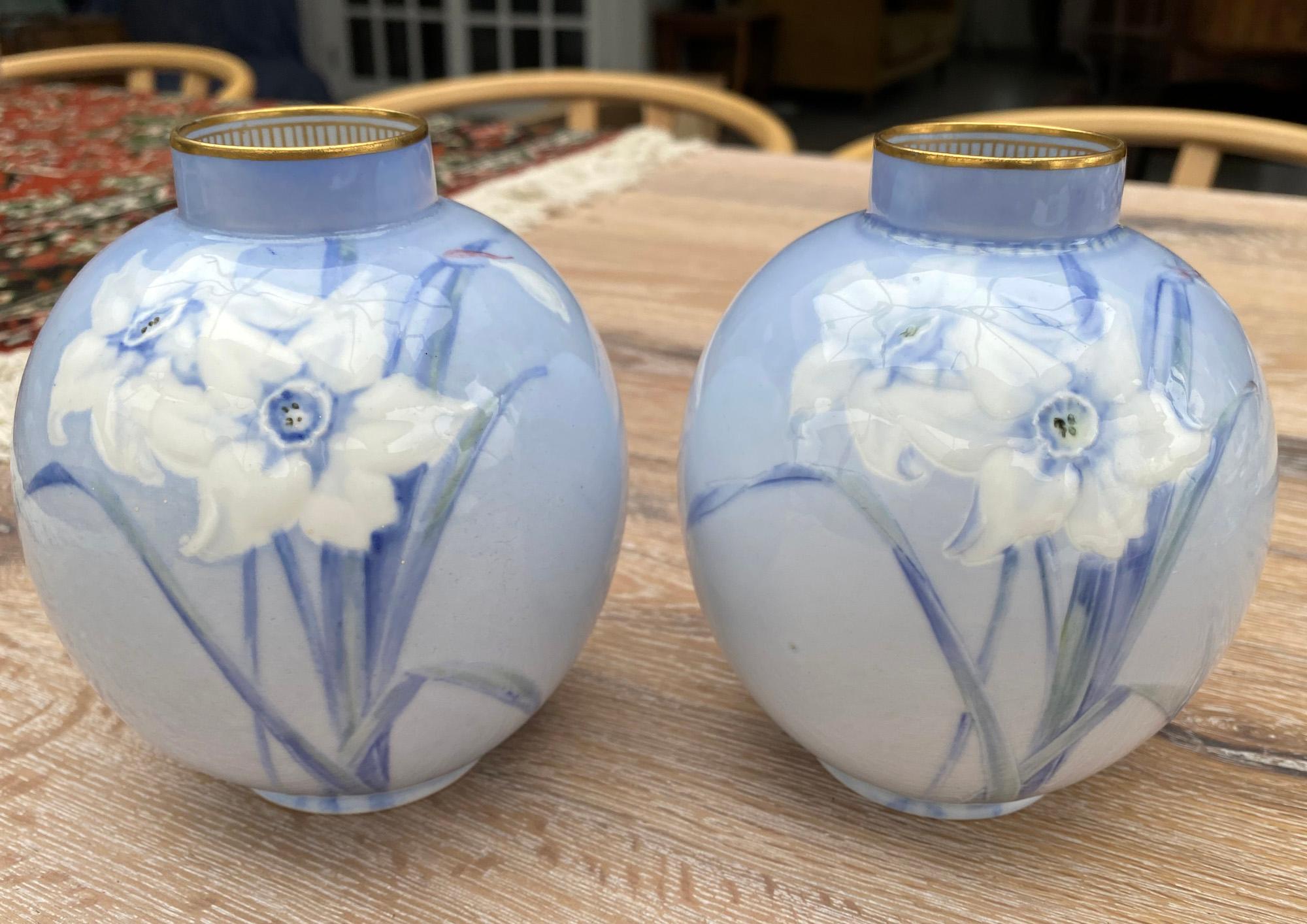 A fine pair Doulton Burslem porcelain vases of rounded bulbous shape hand decorated with daffodils in slip and painted designs in white and blue on a light blue ground by Jack Price. The vases have a gilded rim with patterning to the inside rim.