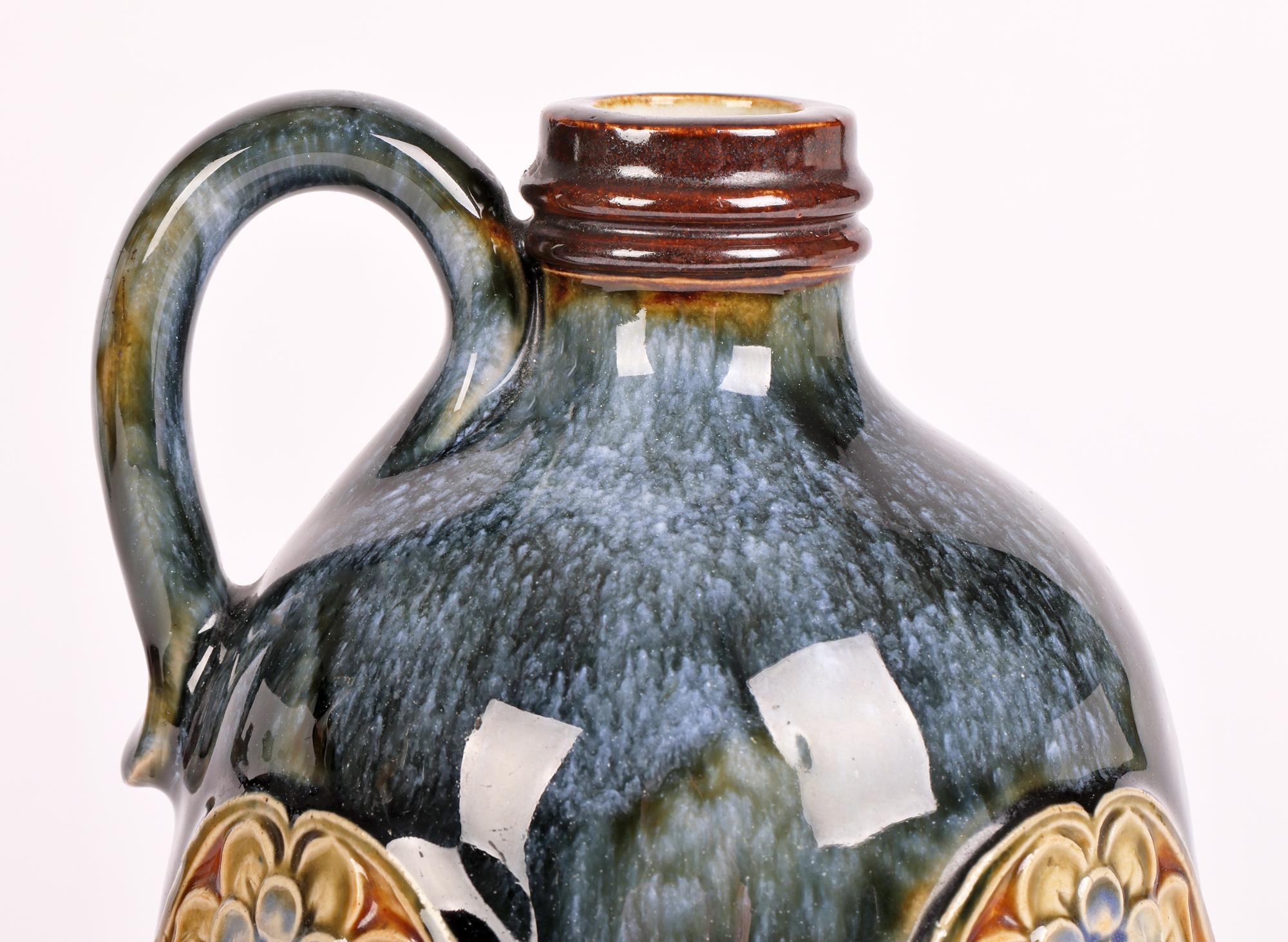A stunning Doulton Lambeth Art Nouveau handled flask with stylized floral panels dating from around 1905. The stoneware flask is of gourd or pear shape standing on a flat narrow round base with a wide lower body and narrow shaped upper body with a