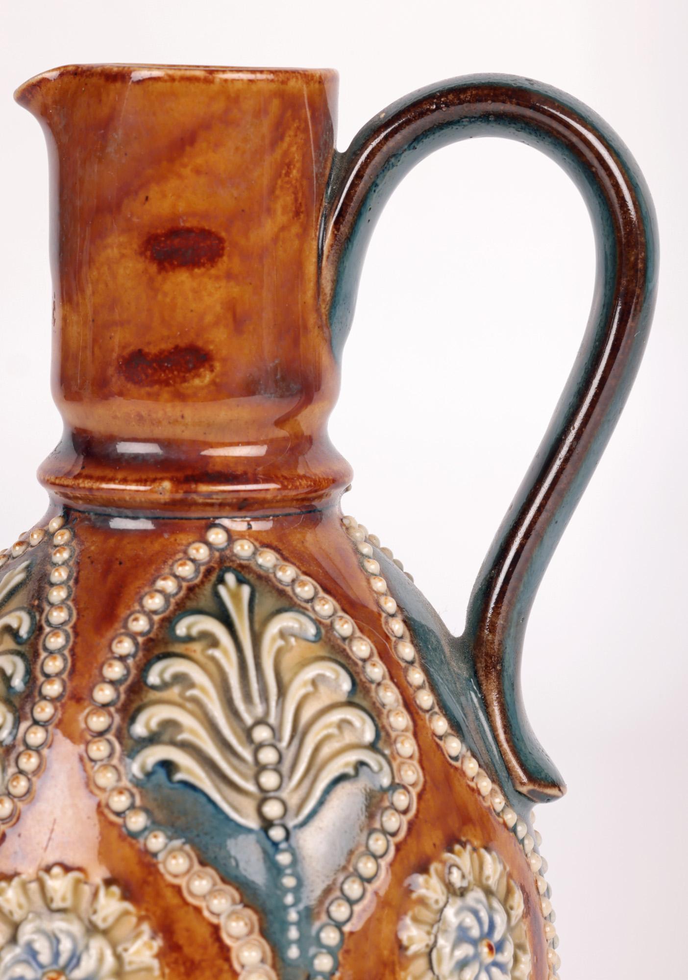 A very stylish Art Nouveau Doulton Lambeth jug decorated with leaf and floral designs by renowned junior artists Annie Partridge and Georgian Pearson and dating from around 1905. The stoneware jug stands raised on a wide round foot with a round