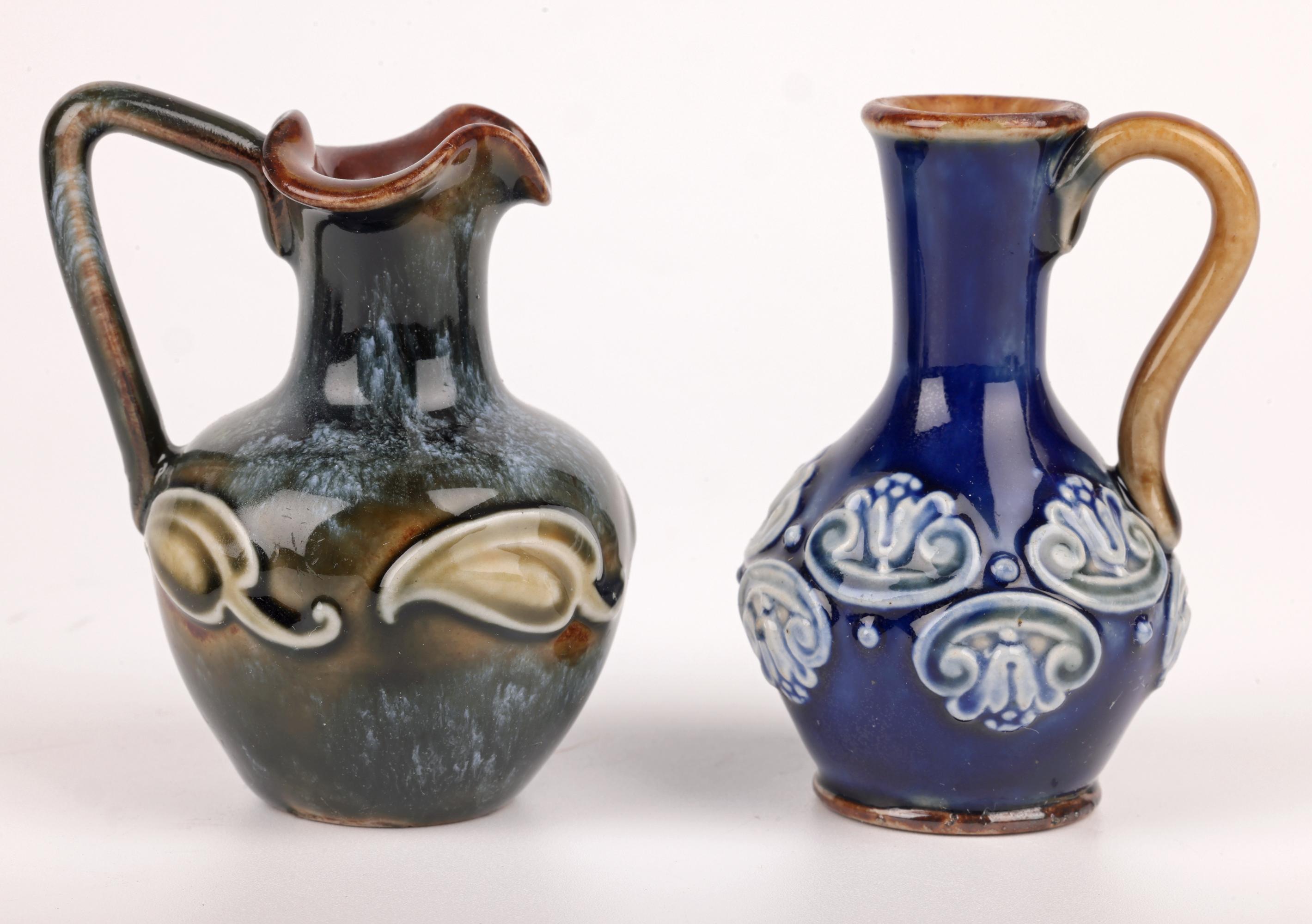 A delightful collection of eight Doulton Lambeth art pottery miniature vessels in the form of vases and ewers and dating from the latter 19th and early 20th Century. The stoneware vessels vary in shape and style with three small vases, three handled
